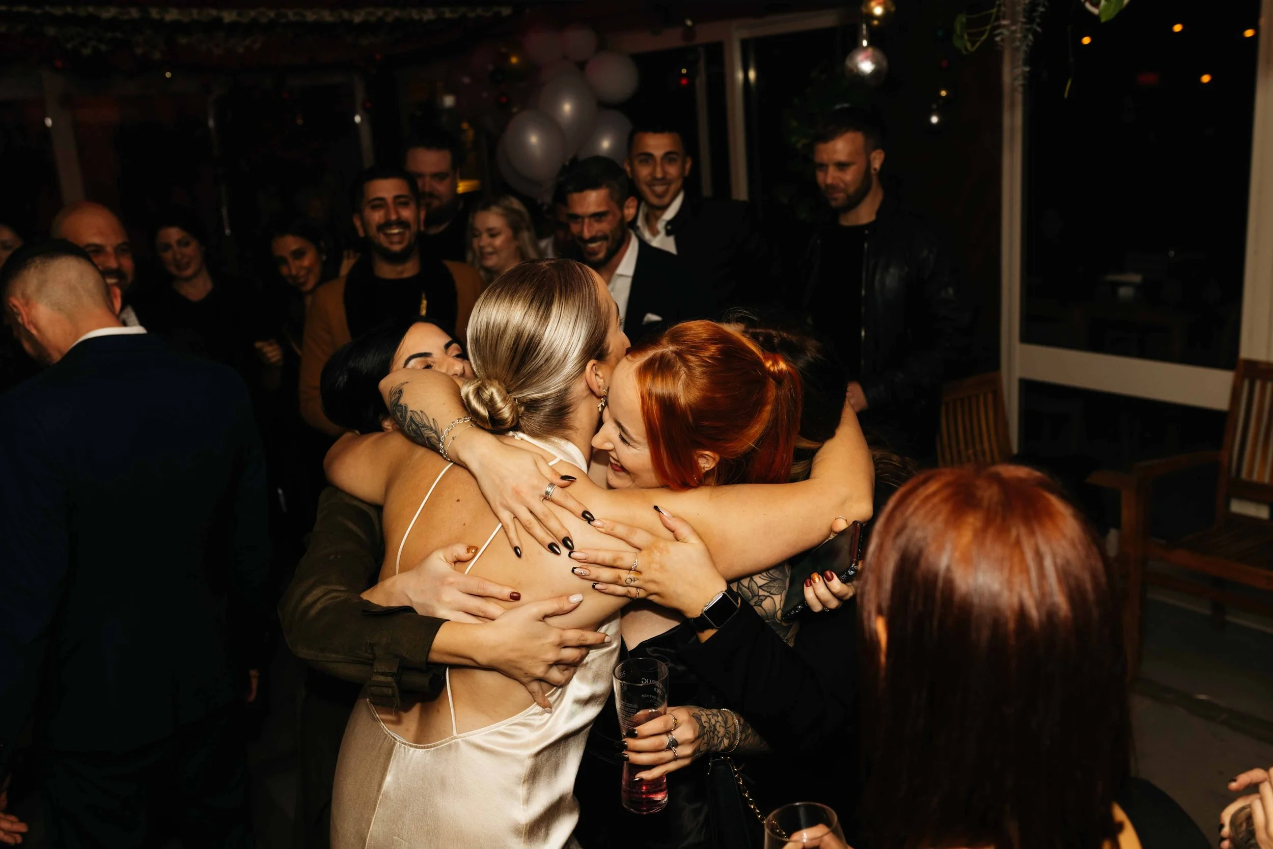 Group of people hugging and celebrating at a party with balloons and festive atmosphere.