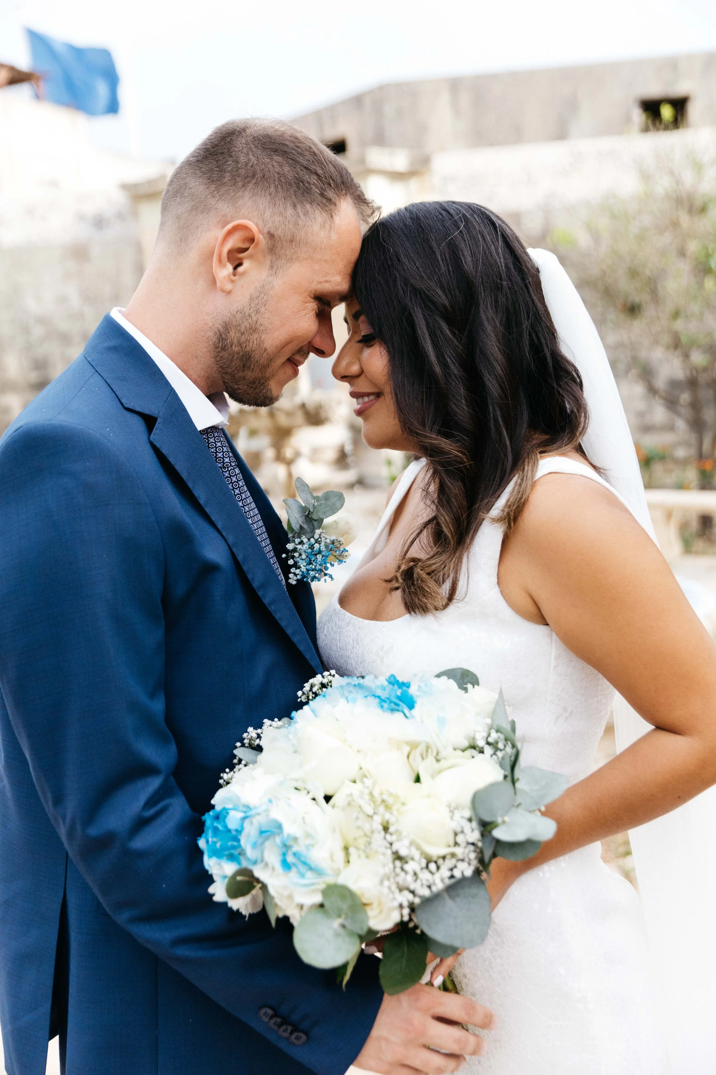 Bride and groom in wedding attire, holding bouquet, outdoors.