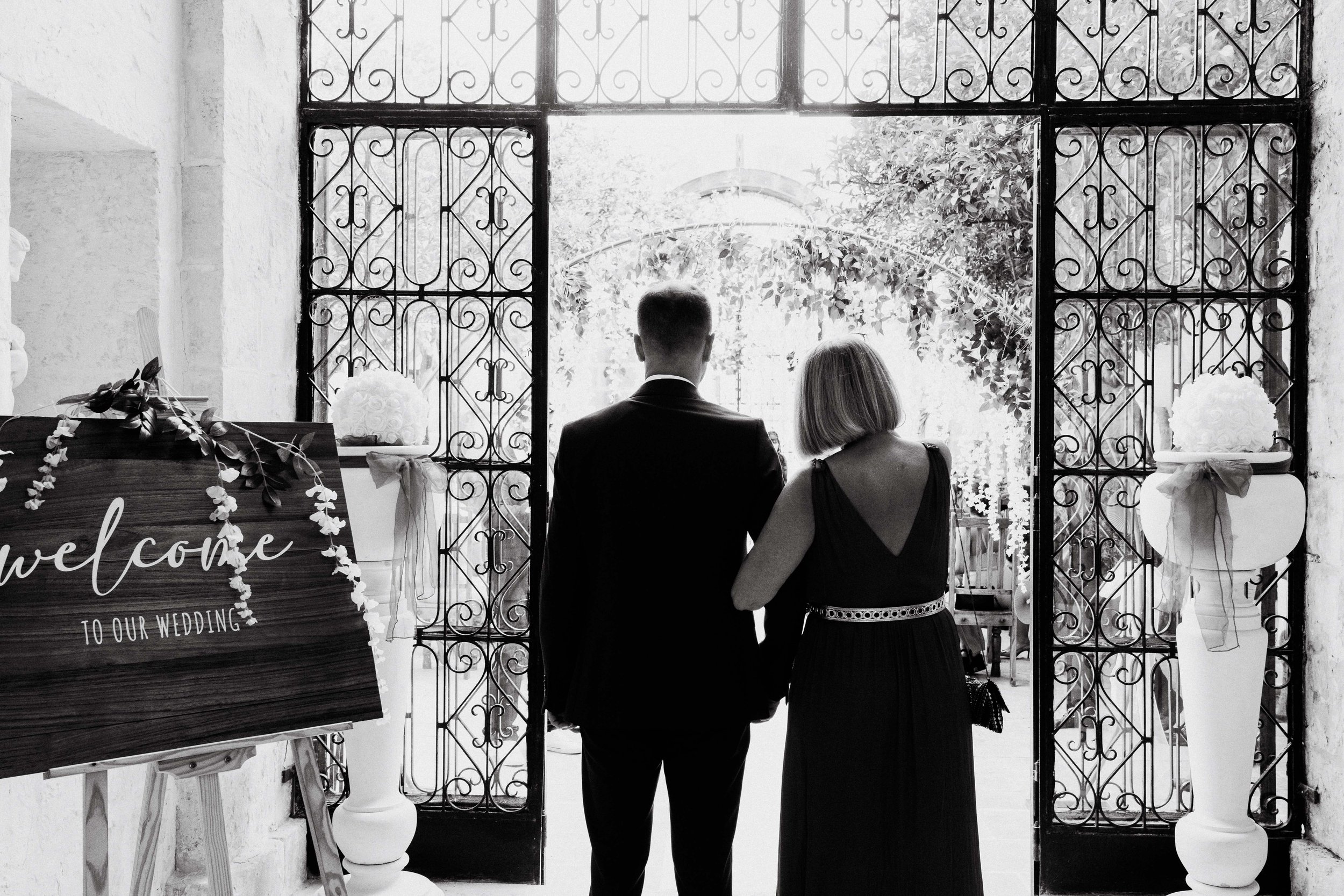 Couple entering wedding venue, decorative sign, floral arrangements, black and white photo