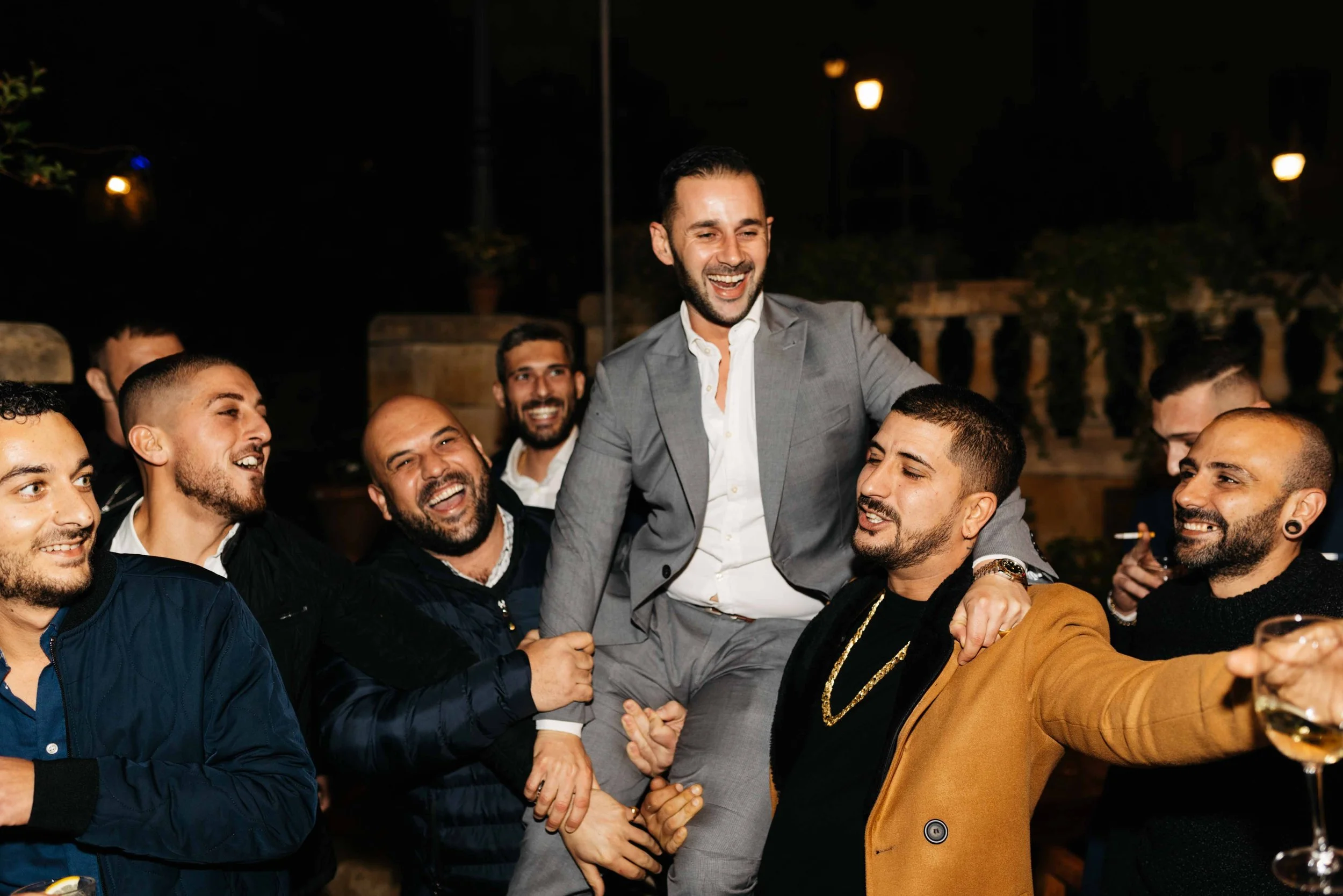 Group of men celebrating at a night event, lifting a man in a suit