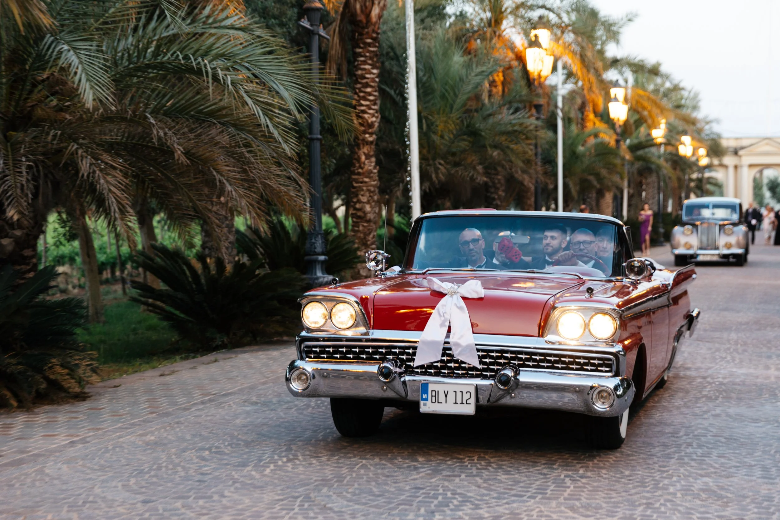 Vintage red convertible with white ribbon driving on palm-lined road