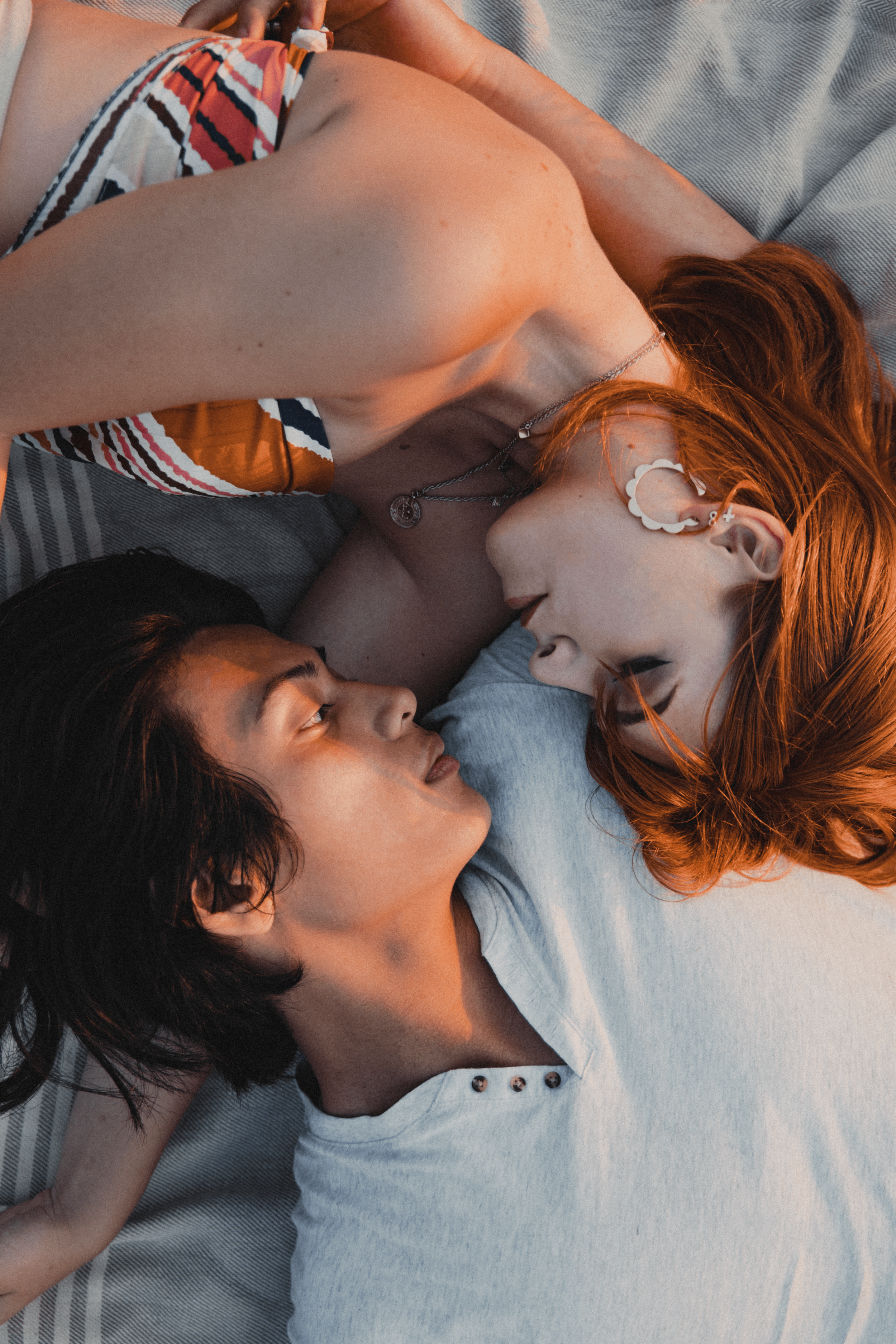 A couple lying on a picnic blanket, facing each other intimately.