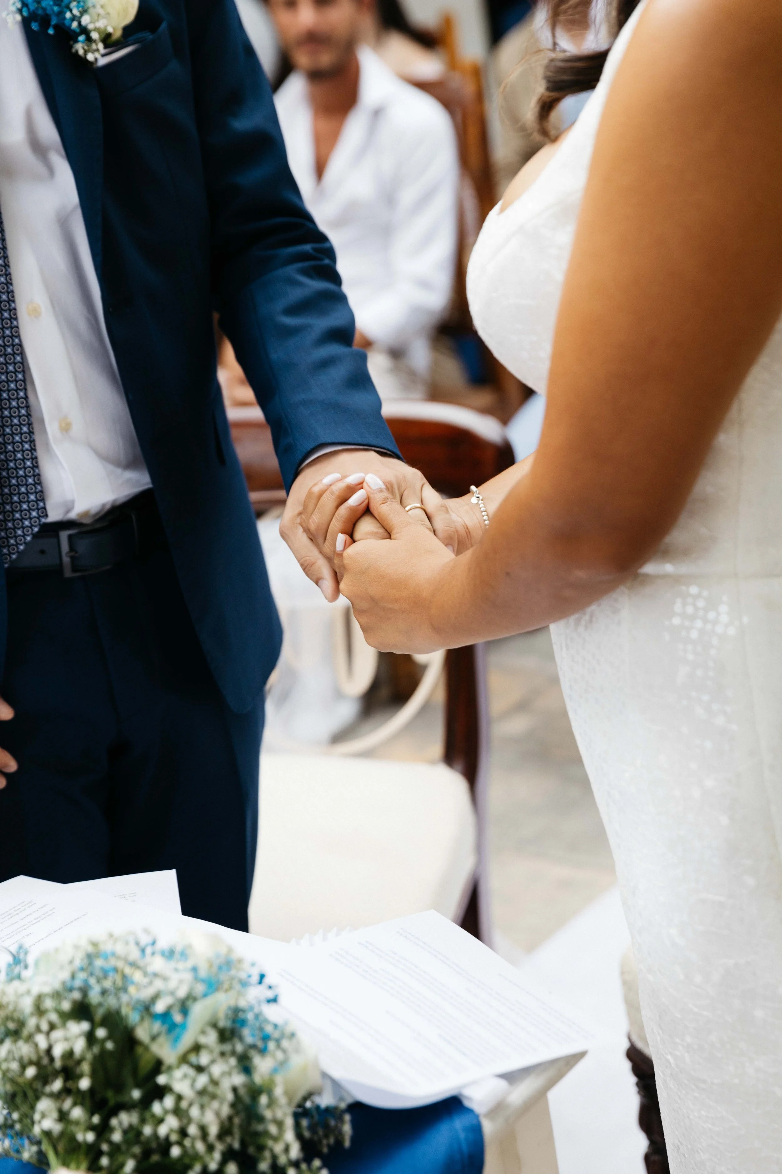 Bride and groom holding hands during wedding ceremony with documents and flower bouquet nearby.
