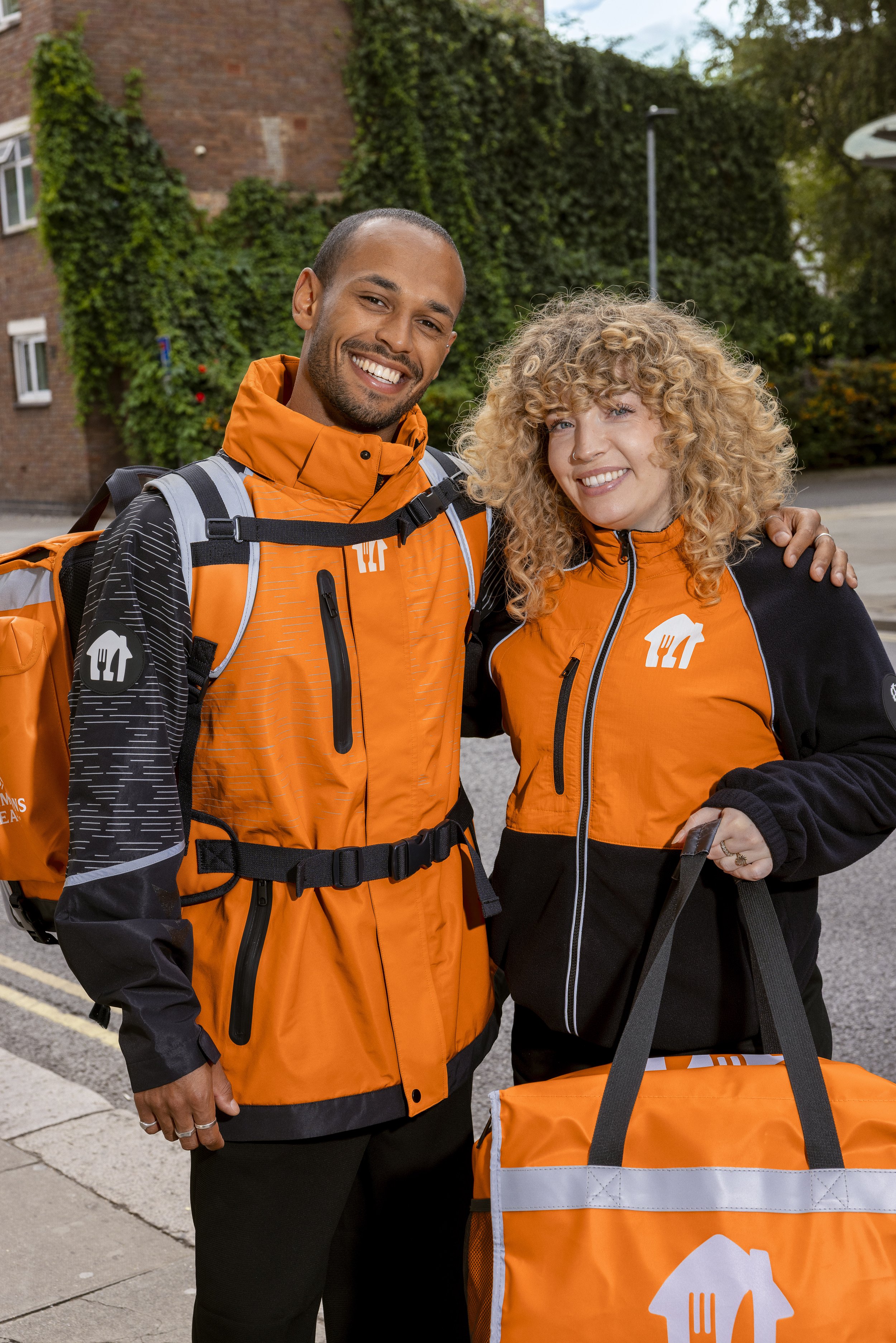 Just Eat campaign: two couriers smiling together on the street with a delivery bag, photographed by Dean Bartolo.