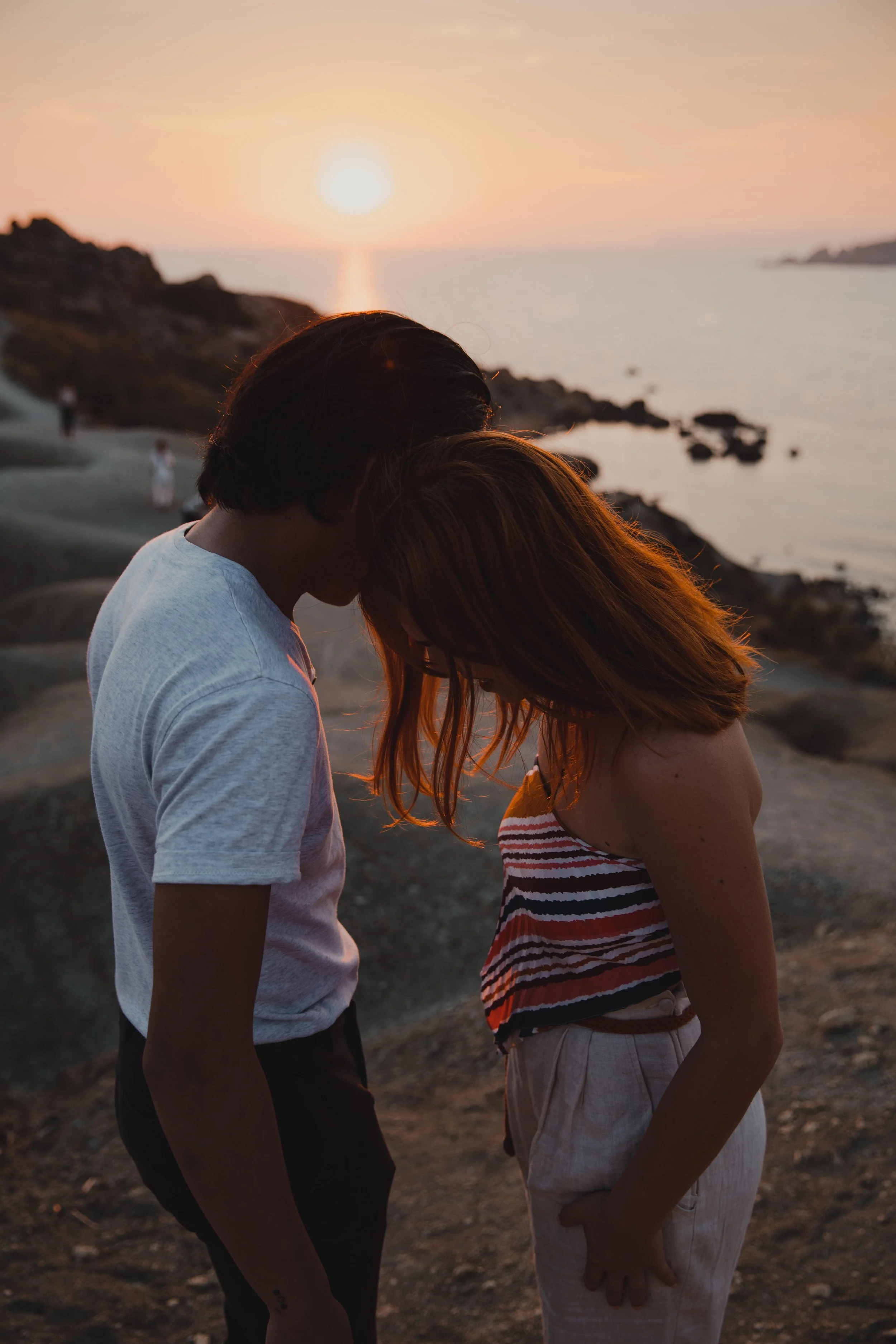Couple standing close at sunset on a rocky beach.