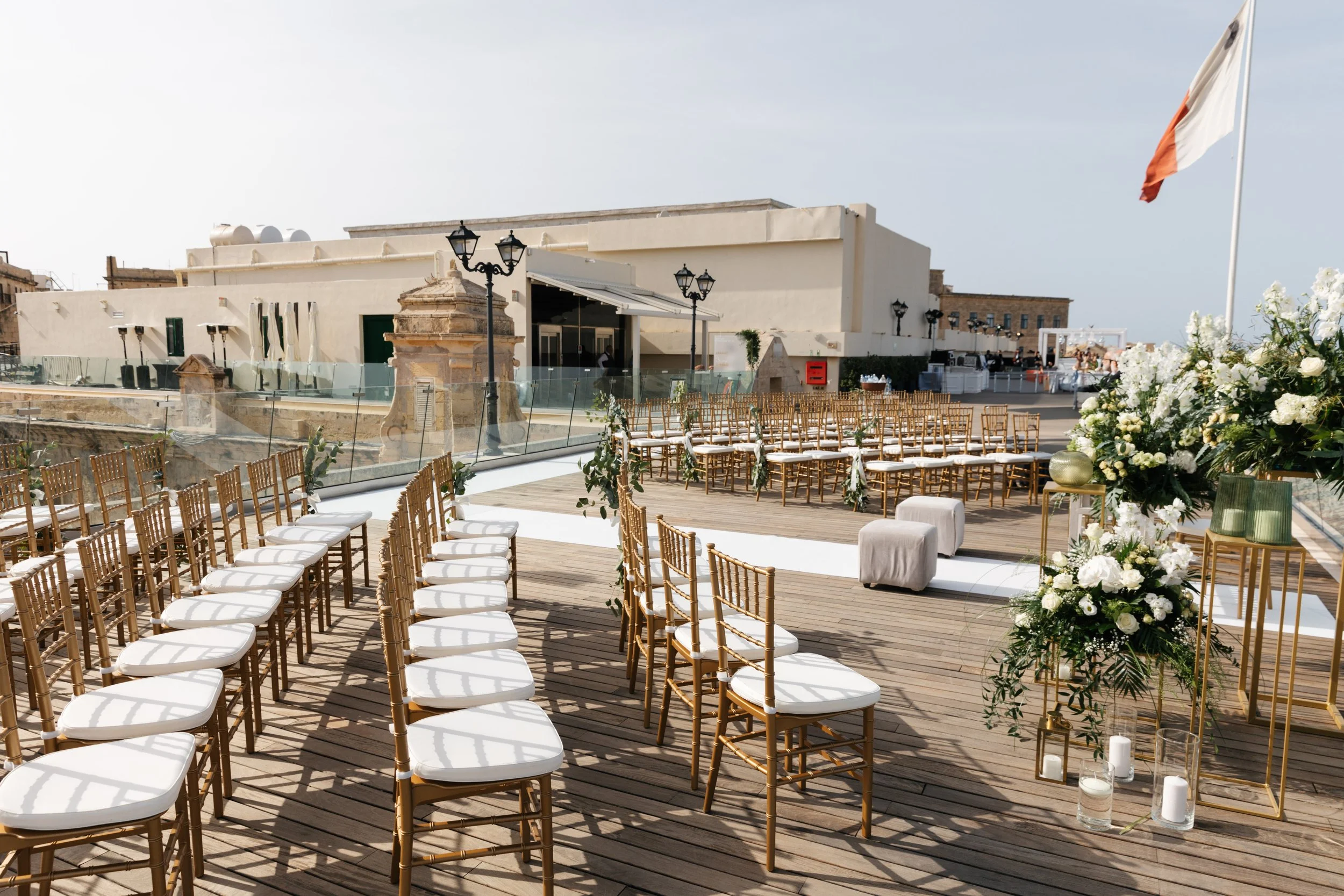 Outdoor wedding ceremony setup with rows of chairs, floral arrangements, and a flag in the background.
