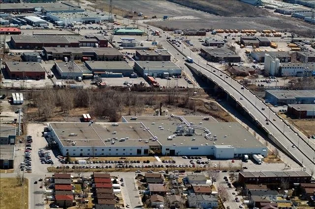 Aerial view of an industrial area with warehouses, a parking lot filled with cars, and a residential neighborhood with houses.