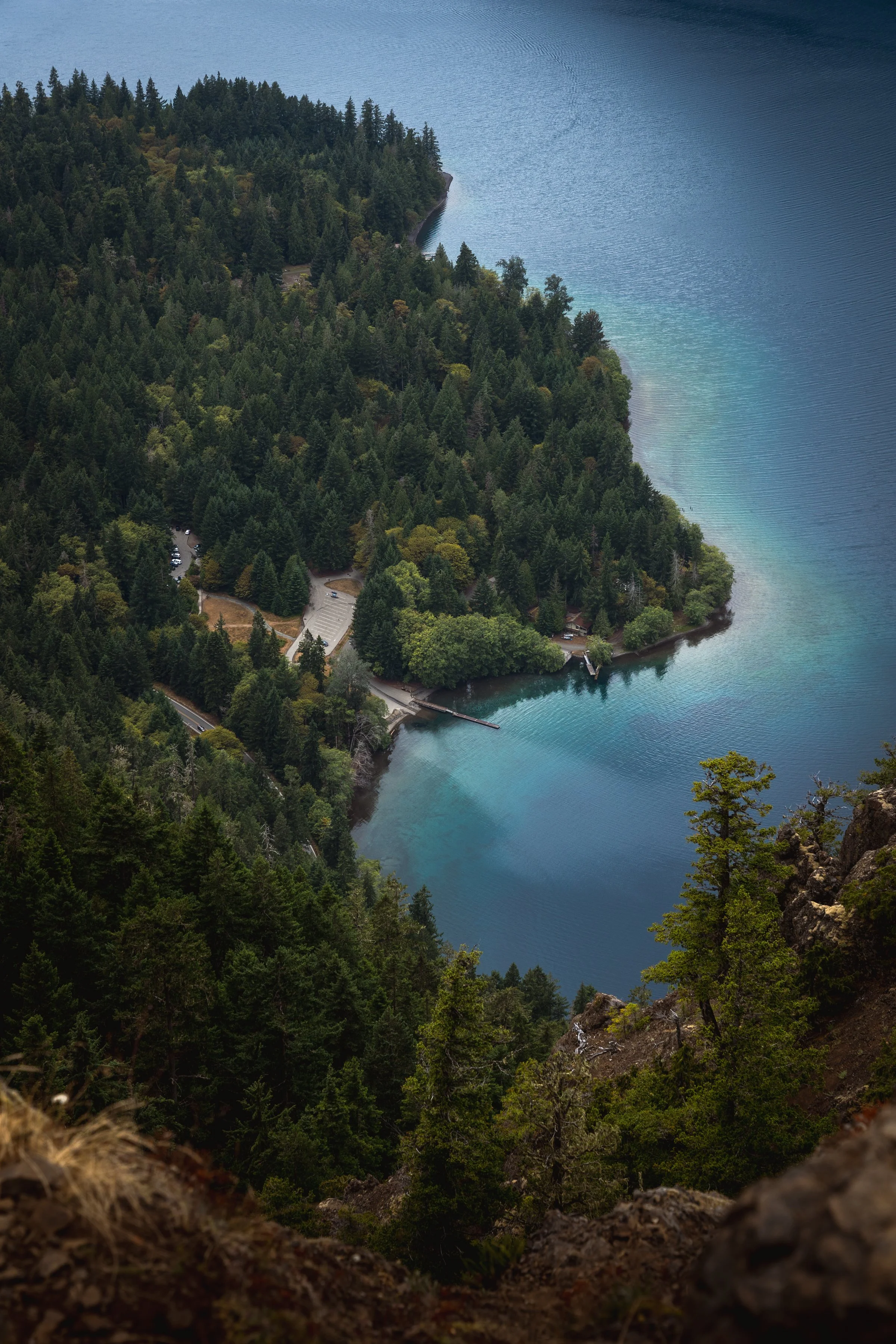 A view of a lake surrounded by dense forest with a rocky overlook in the foreground.