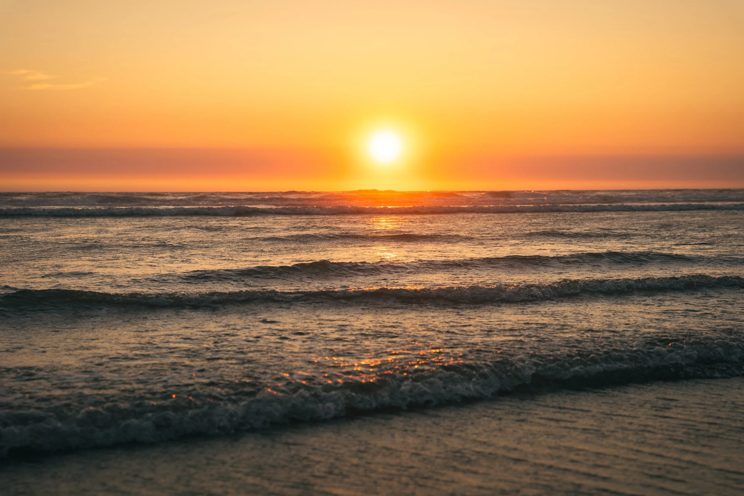 Sunset over the ocean with waves gently crashing on the shore.