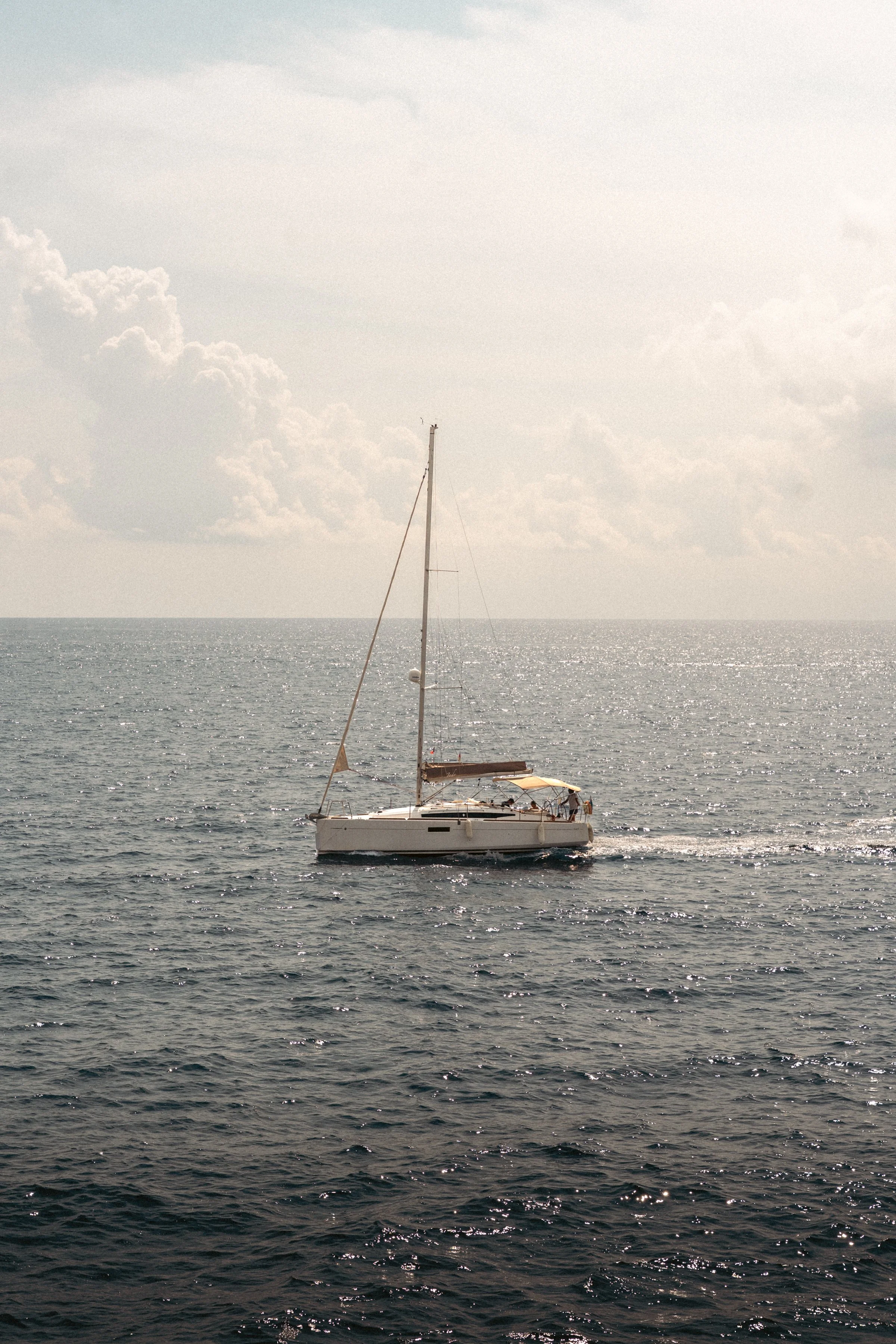 A sailboat floating on calm ocean waters with a partly cloudy sky.