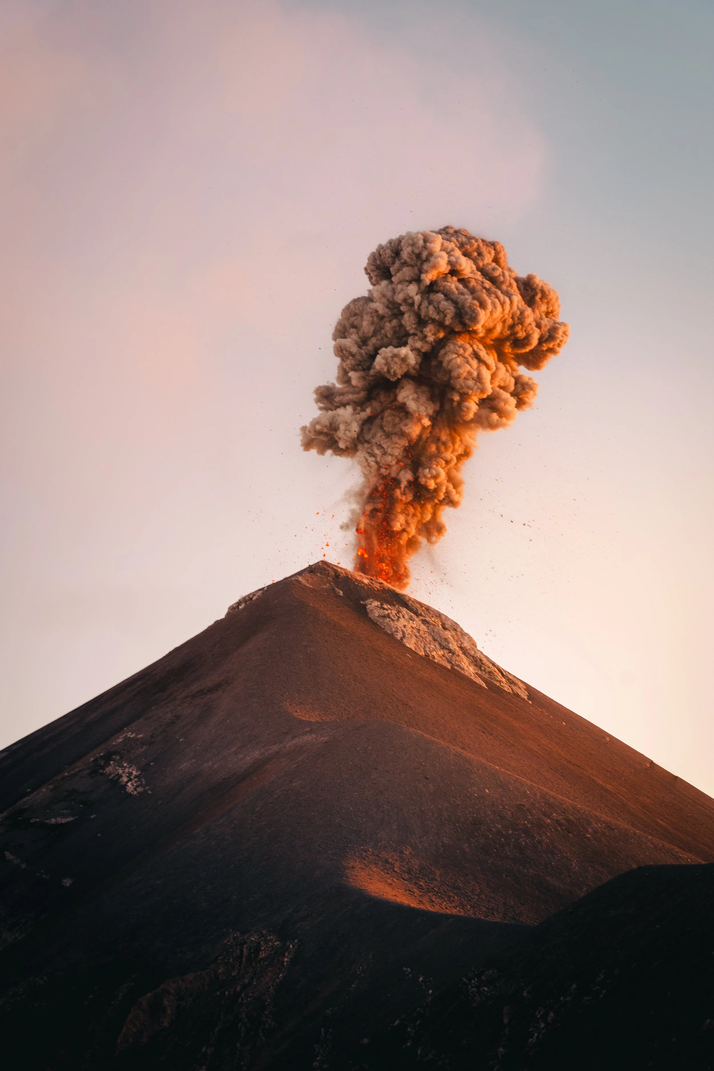 A volcano erupting with ash and lava spewing from its summit against a pastel sky.