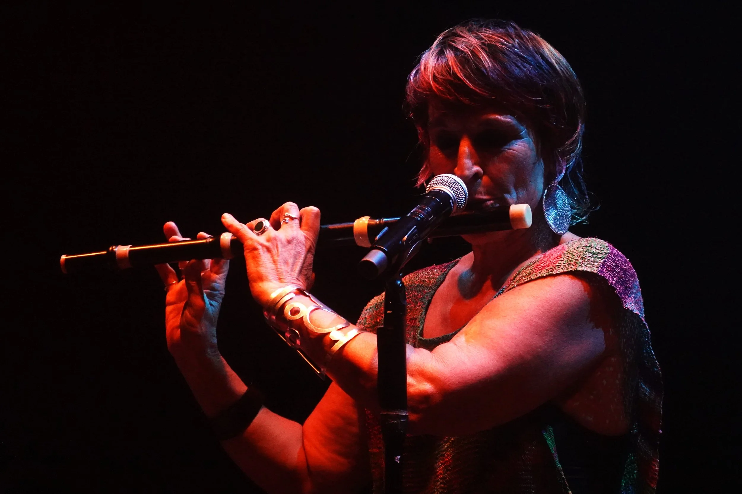 Femme jouant de la flûte lors d'un concert, sous un éclairage sombre avec des lumières colorées.