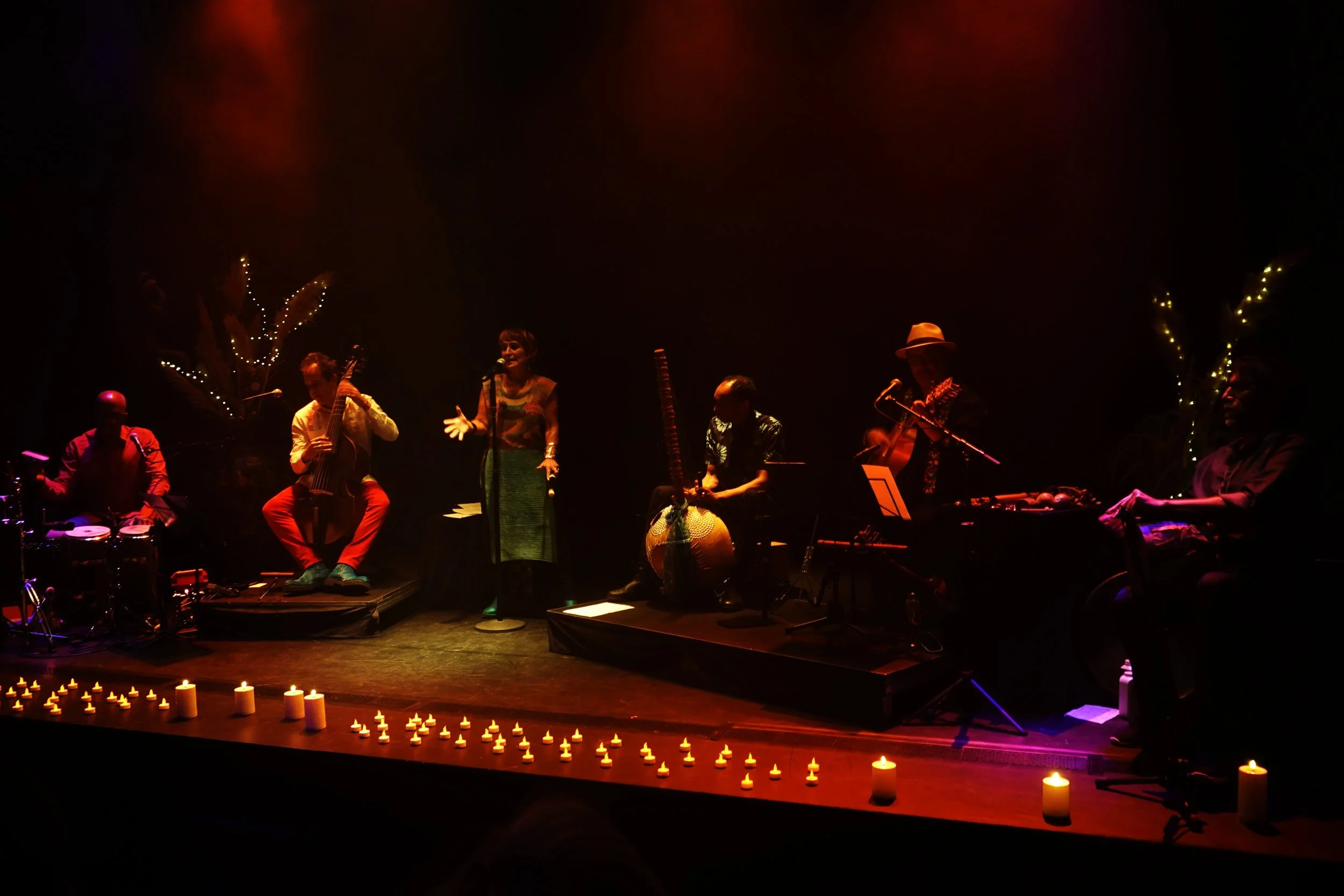Groupe de musiciens jouent sur scène avec des bougies devant. La scène est sombre avec des lumières chaudes.