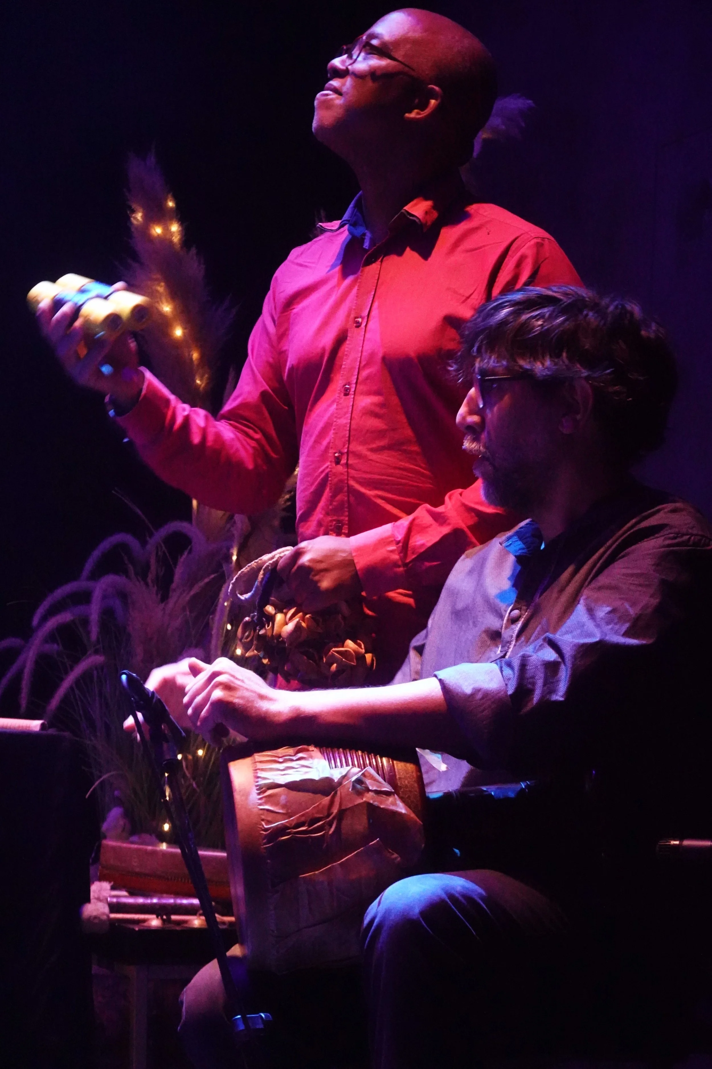 Deux hommes jouent de la musique avec un instrument à percussion, dans une ambiance tamisée avec des lumières colorées