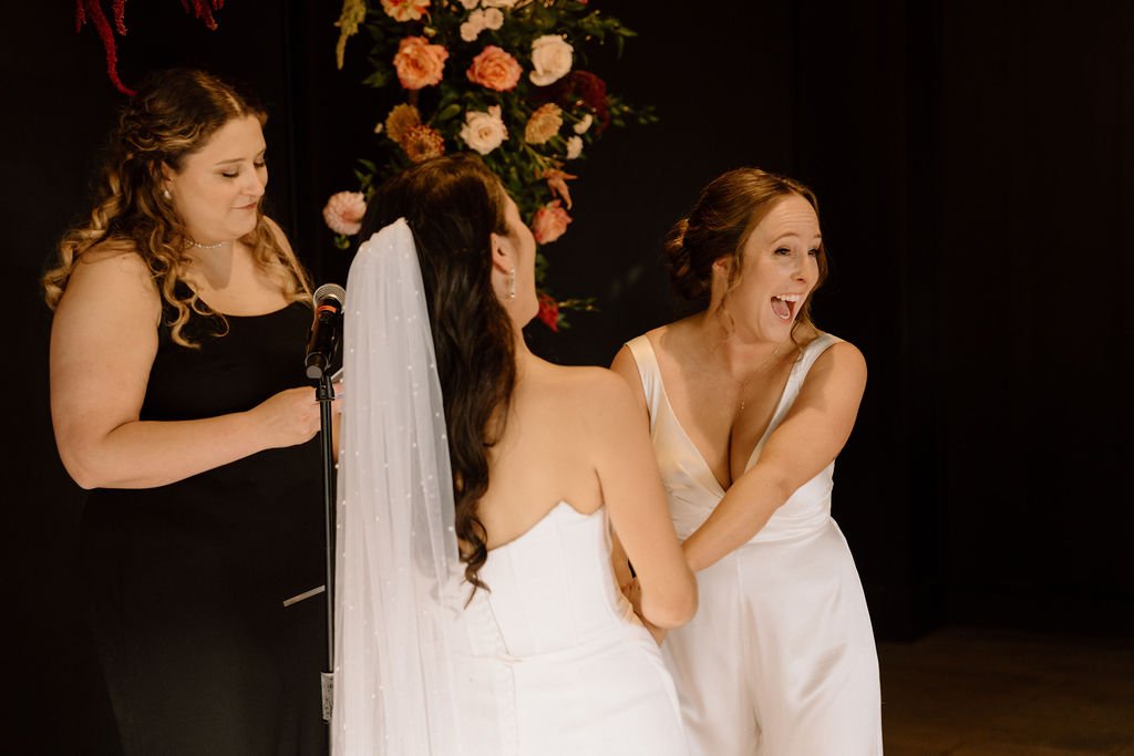 candid moment of brides laughing during their wedding ceremony at the ivy at ellis preserve