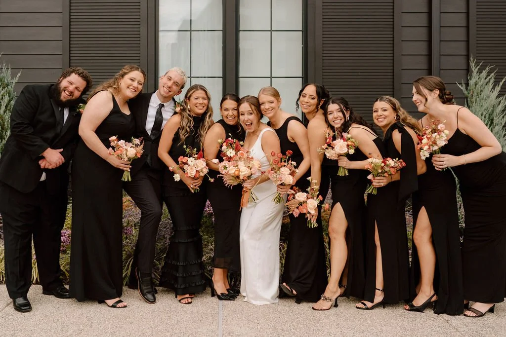 wedding couple and all-black wedding party posing outdoors at the ivy at ellis preserve