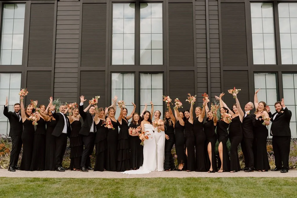 wedding couple and all-black wedding party posing outdoors at the ivy at ellis preserve