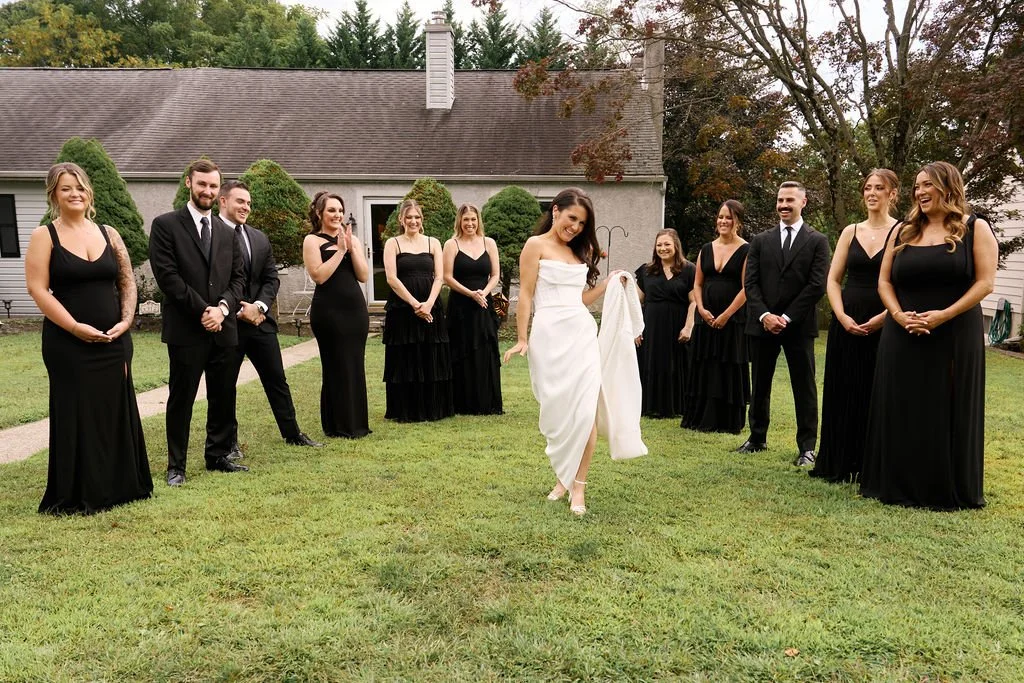 wedding couple and all-black wedding party posing outdoors at the ivy at ellis preserve