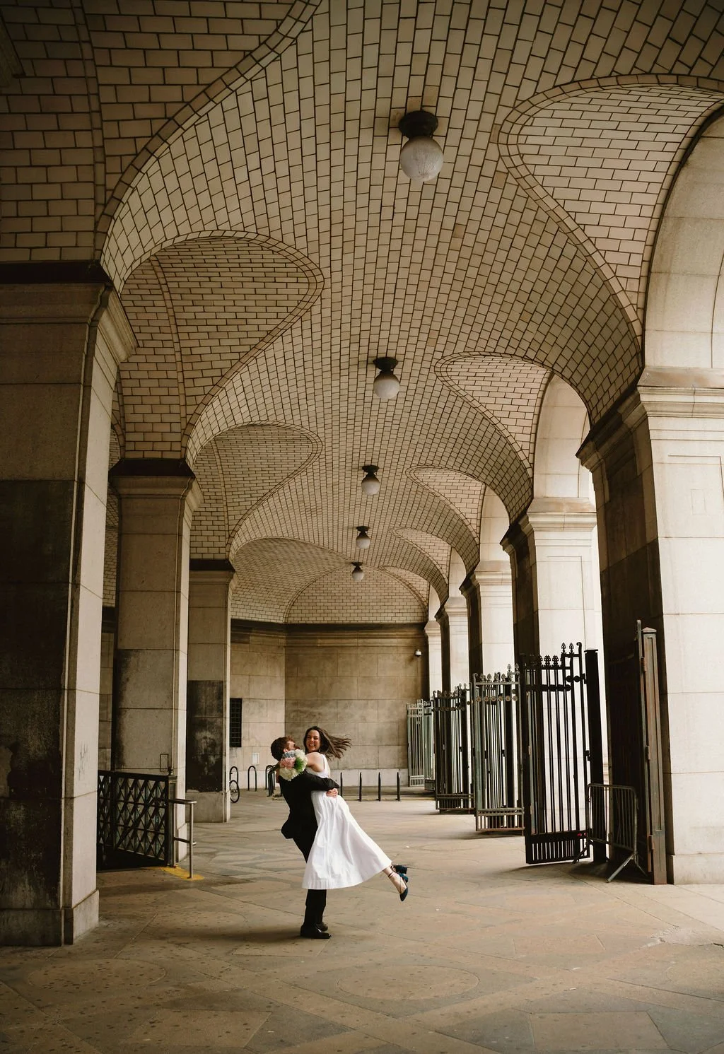 Bride and groom posing beneath the stone archways at New York City Hall following their intimate NYC wedding