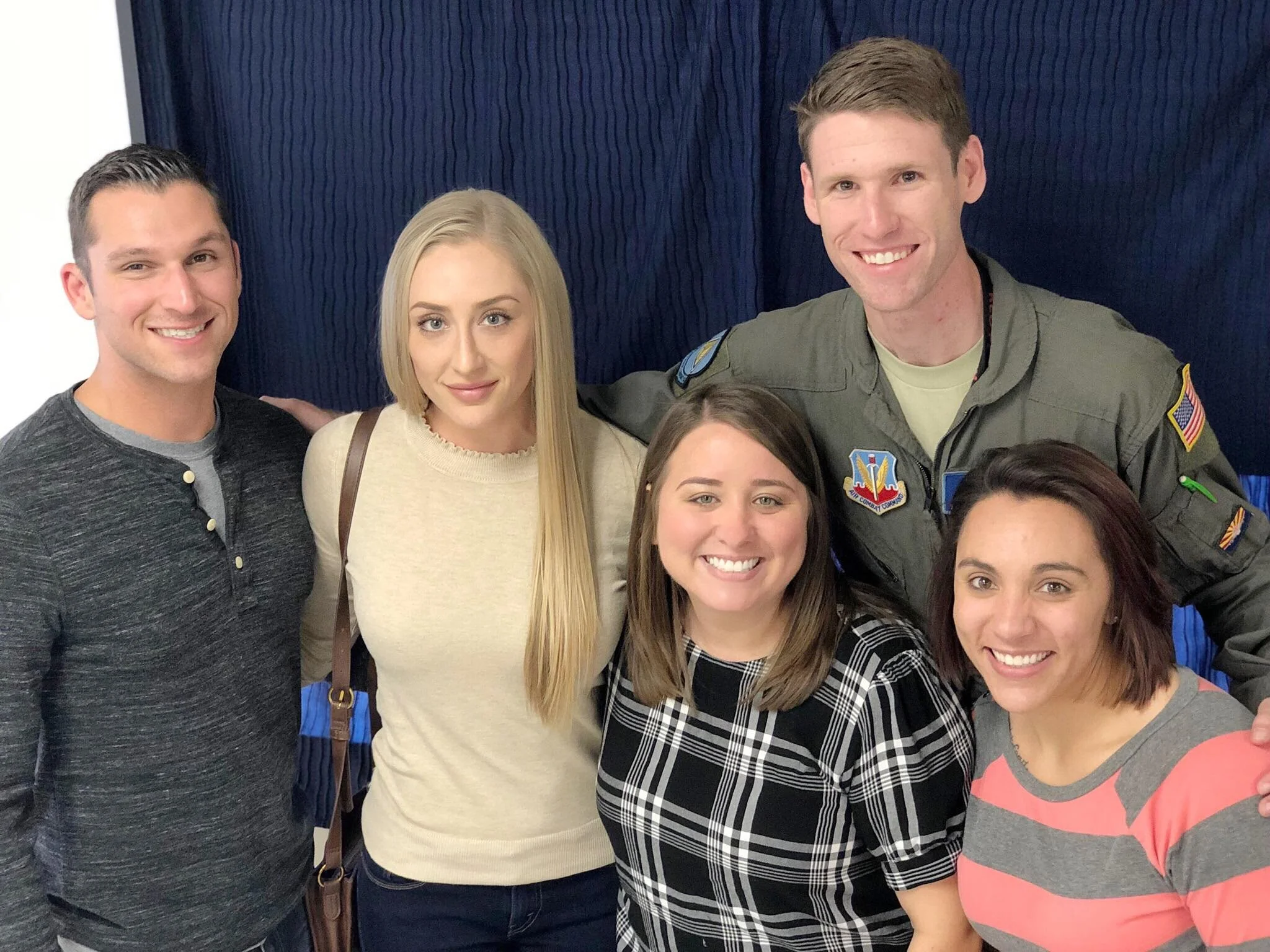 Group of people posing together for a photo, some smiling, in front of a dark blue backdrop.