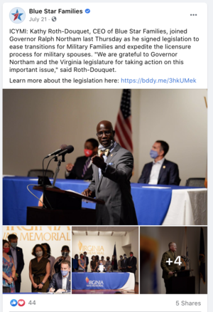 Photo of Kathy Roth-Douquet, CEO of Blue Star Families, speaking at a podium during a press event, with an American flag in the background. Several people, some wearing masks, are seated at a table and standing around, attending the event.