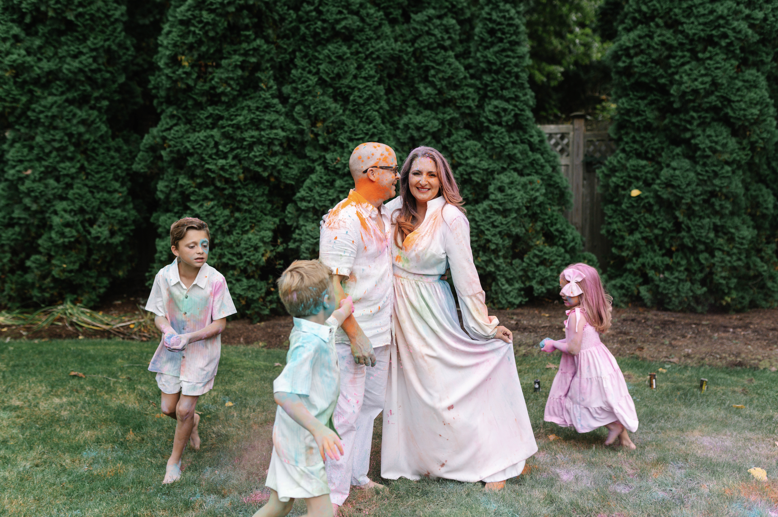 People celebrating a colorful Easter egg hunt, covered in splashes of bright colors, in a backyard with green bushes.