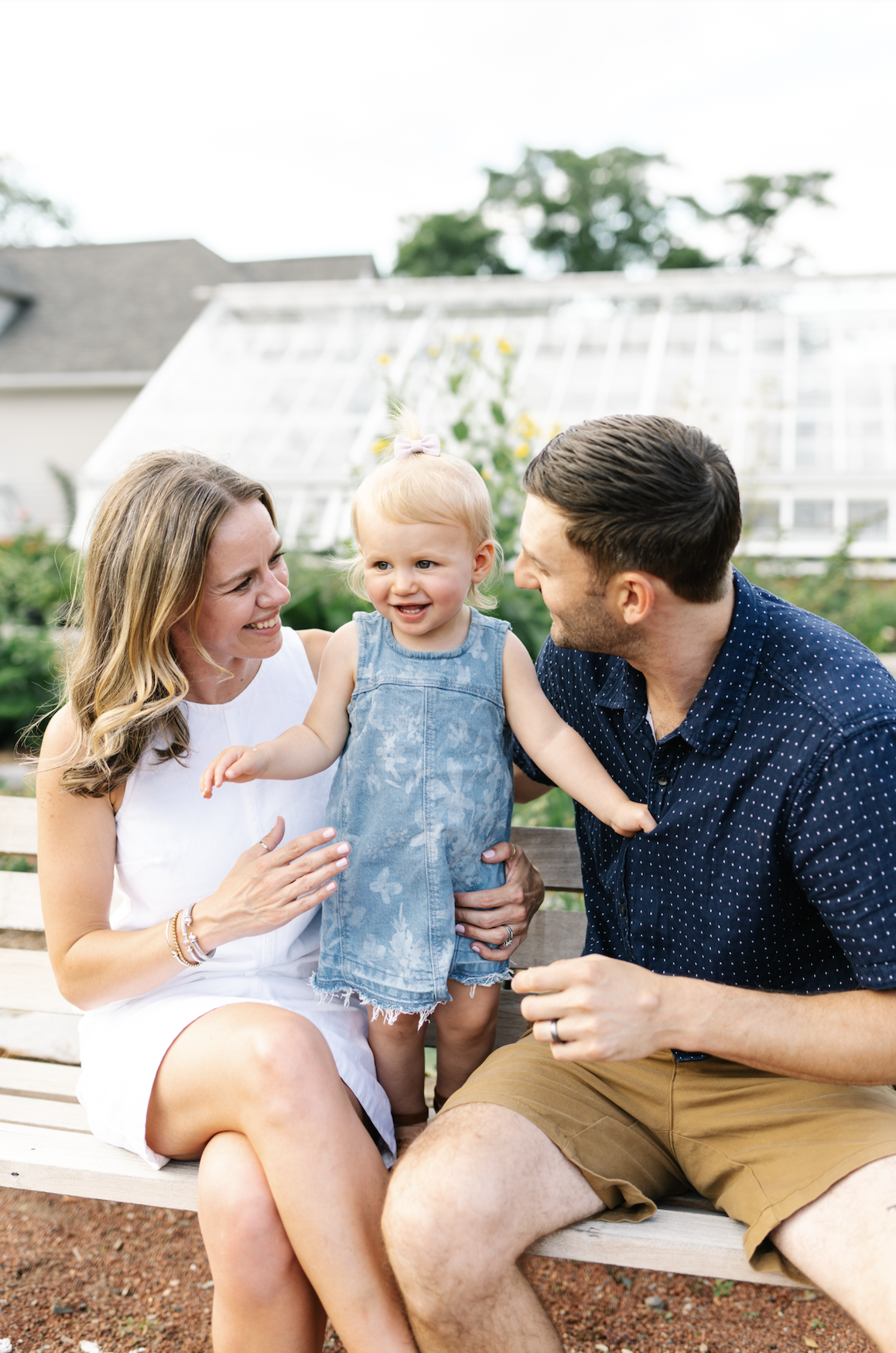 A happy family of three, including a woman, a man, and a young girl, sitting on a park bench outdoors, smiling and enjoying each other's company.