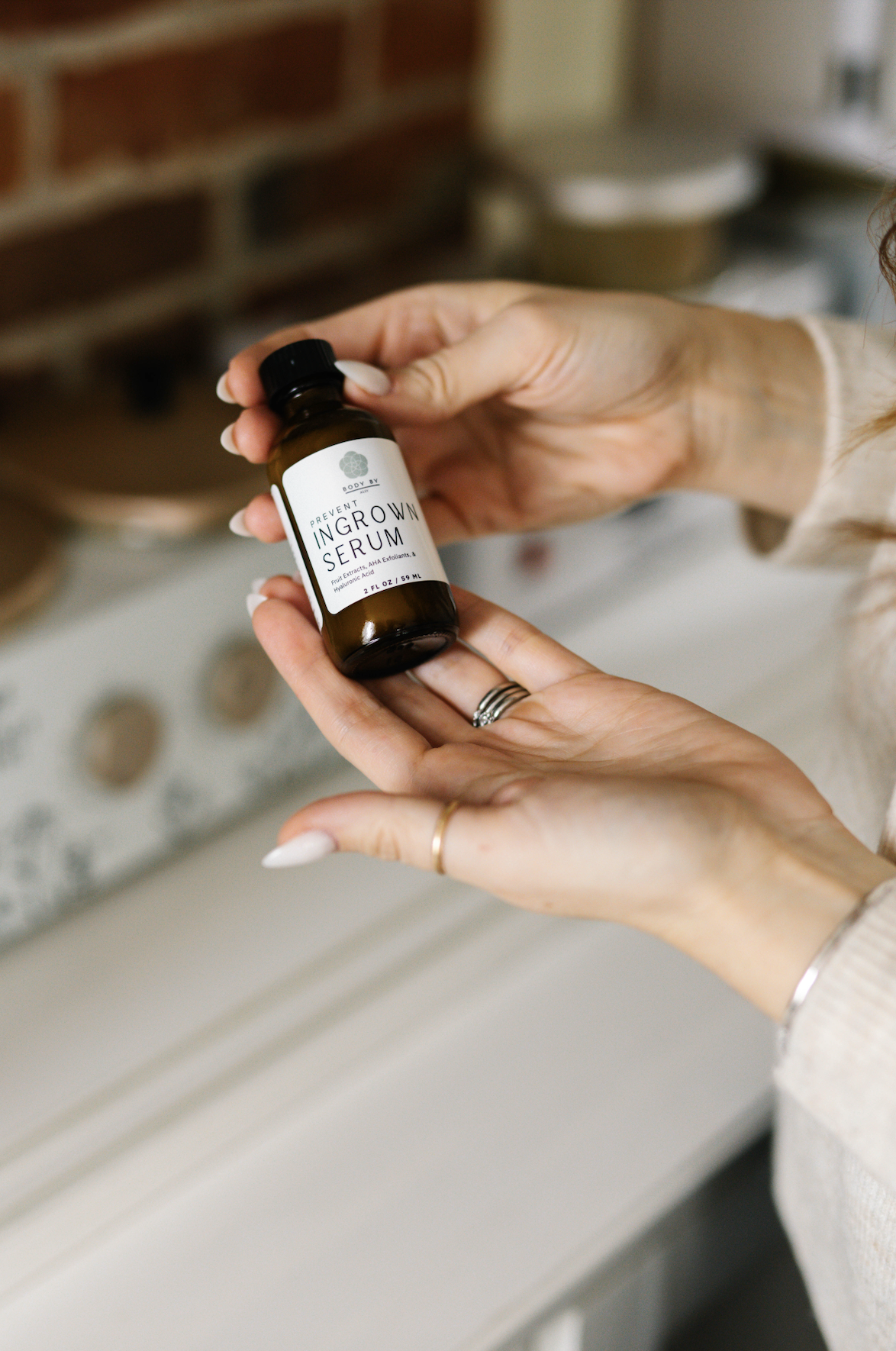 Person holding a small bottle labeled 'Prevent Ingrown Serum' in a cozy, well-lit room.