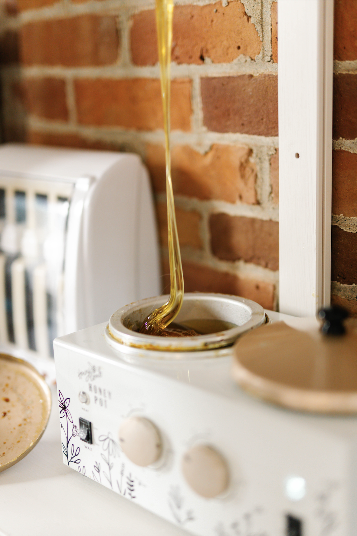 Honey being poured into a honey pot on a white countertop, with a brick wall in the background.