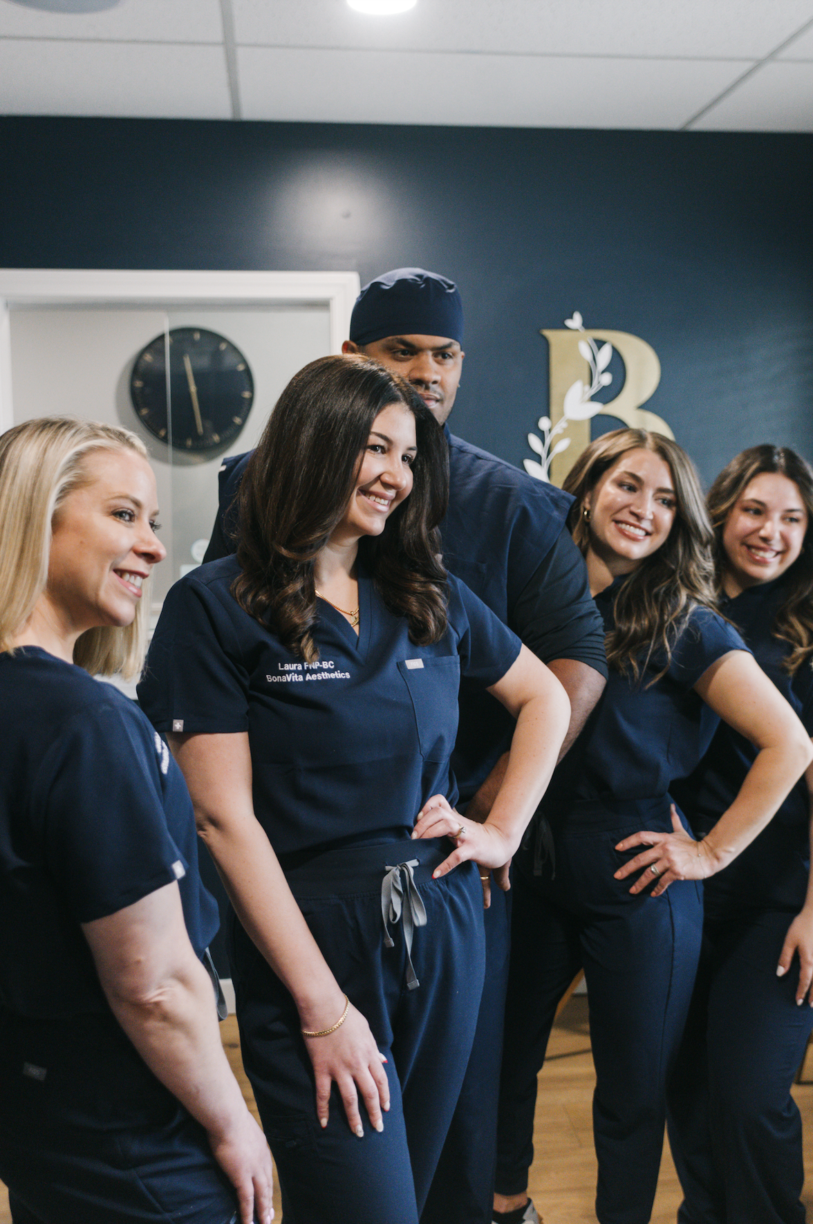 Group of healthcare professionals in navy scrubs, smiling and posing in a medical office or clinic.