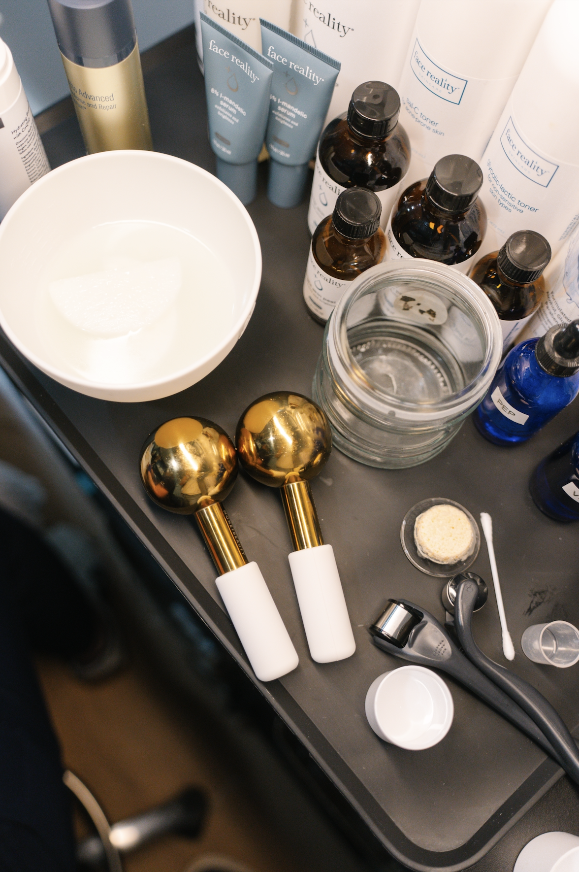 Beauty and skincare tools and products on a black tray, including massage rollers, bottles, jars, and skincare tubes.