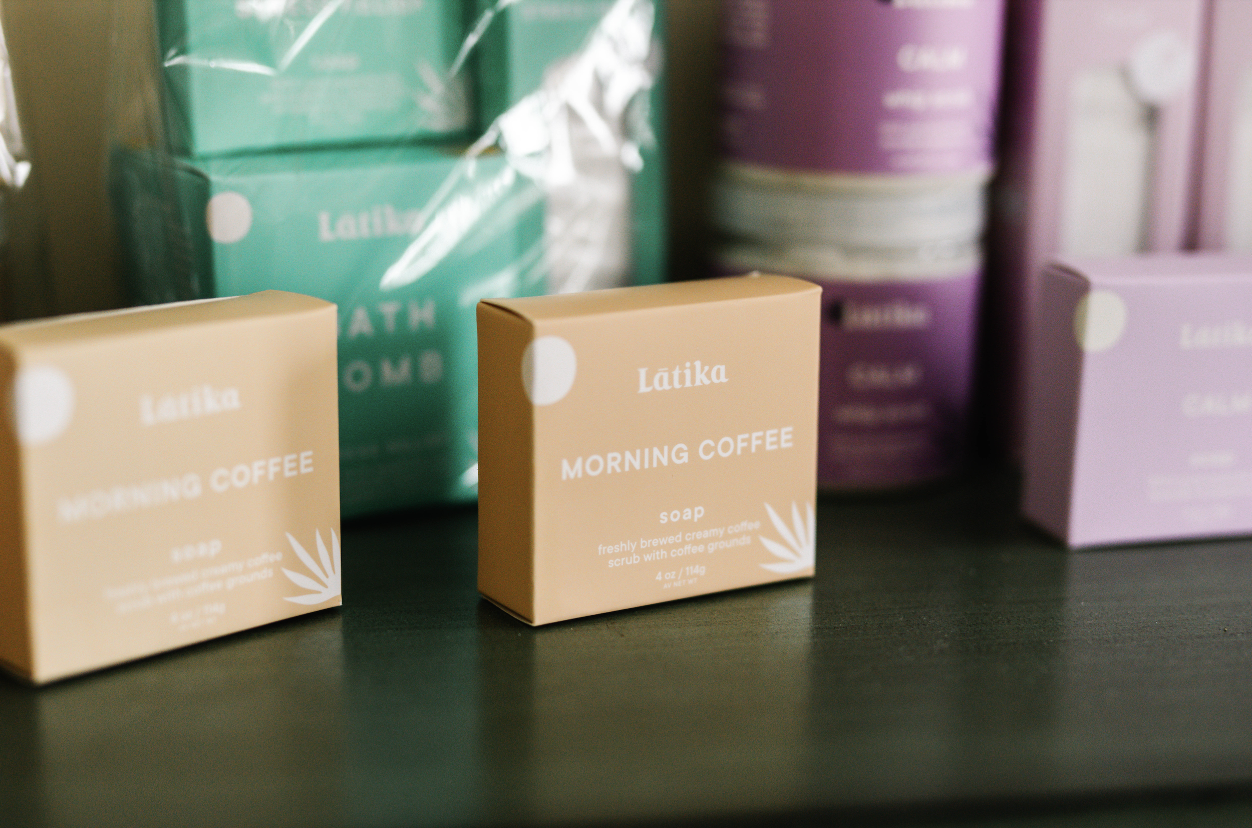 Close-up of colorful packaged products with a focus on a beige box labeled 'Latika Morning Coffee soap' and other similar packages in pastel shades in the background.