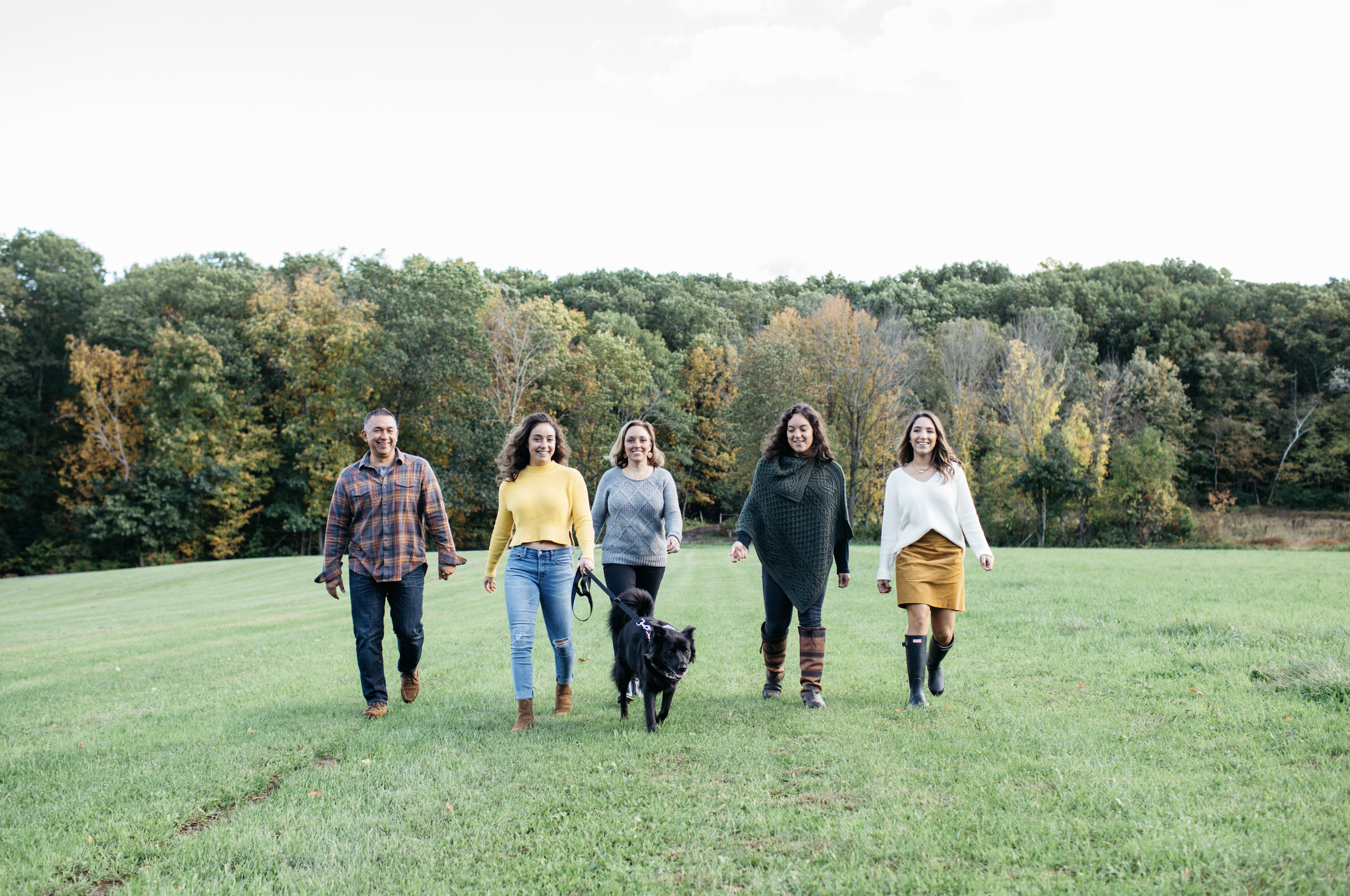 Group of five people walking on a grassy field with a dog, trees in the background, during daytime.
