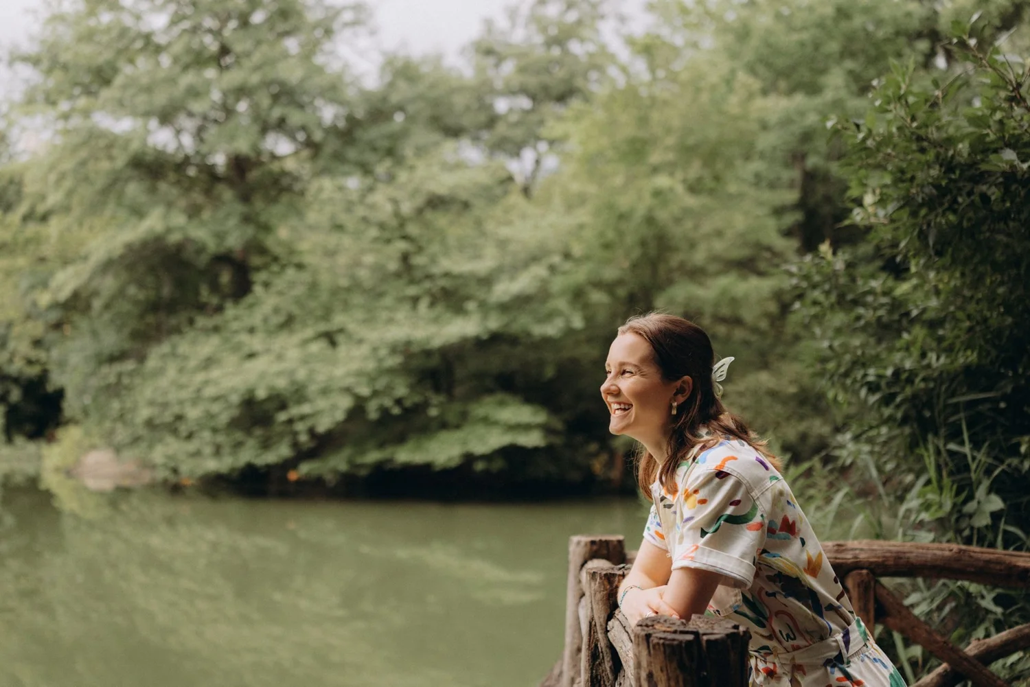 Syd laughing at a wooden railing beside a pond in Central Park