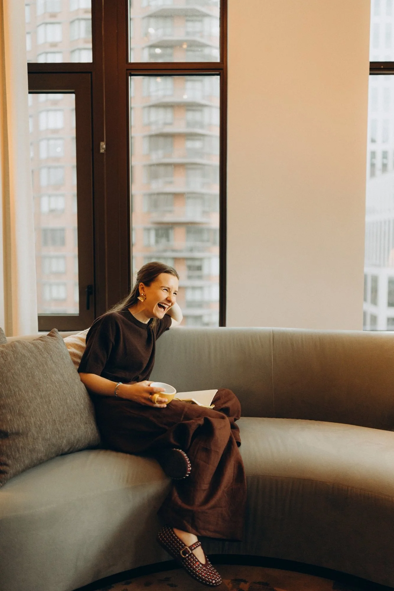 Syd laughing on a curved sofa with a coffee cup