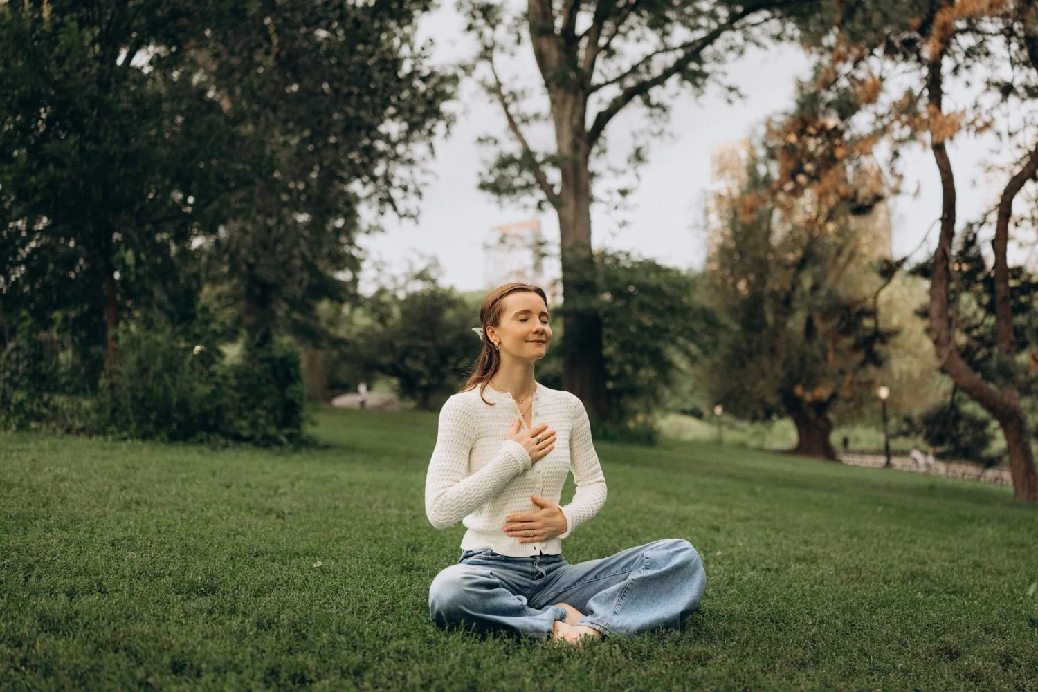 Syd sitting cross-legged on the lawn in Central Park, eyes closed, one hand on her heart