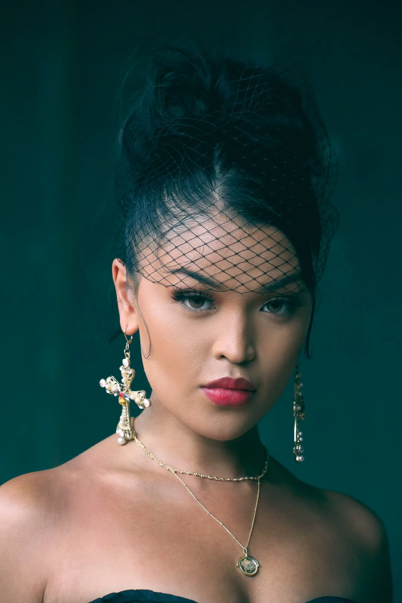 A woman with bold makeup, black veil, and earrings, looking directly at the camera.