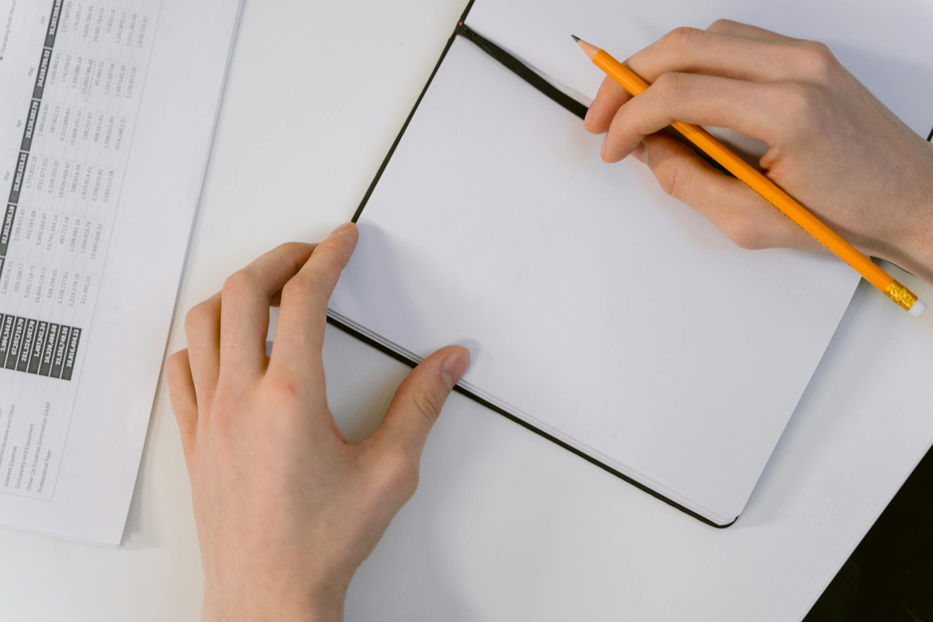 A person's hands holding a pencil over a blank notebook and a calendar, prepared for planning and organization.