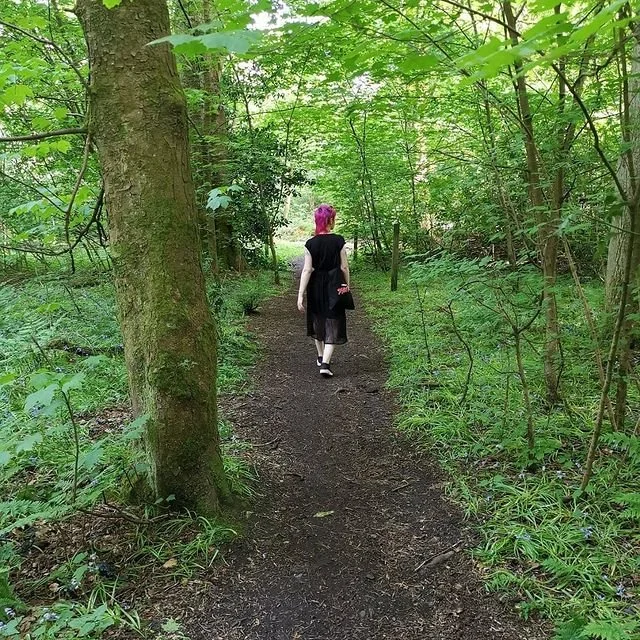 Emma walks away with her back to the camera down a path in the woods