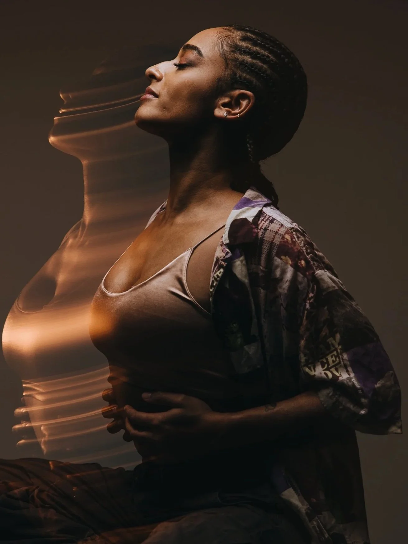 A young woman with closed eyes, sitting with a calm expression, wearing a tank top and a patterned jacket, with her hands resting on her stomach. An artistic, motion-blurred double exposure effect shows a second profile of her face.
