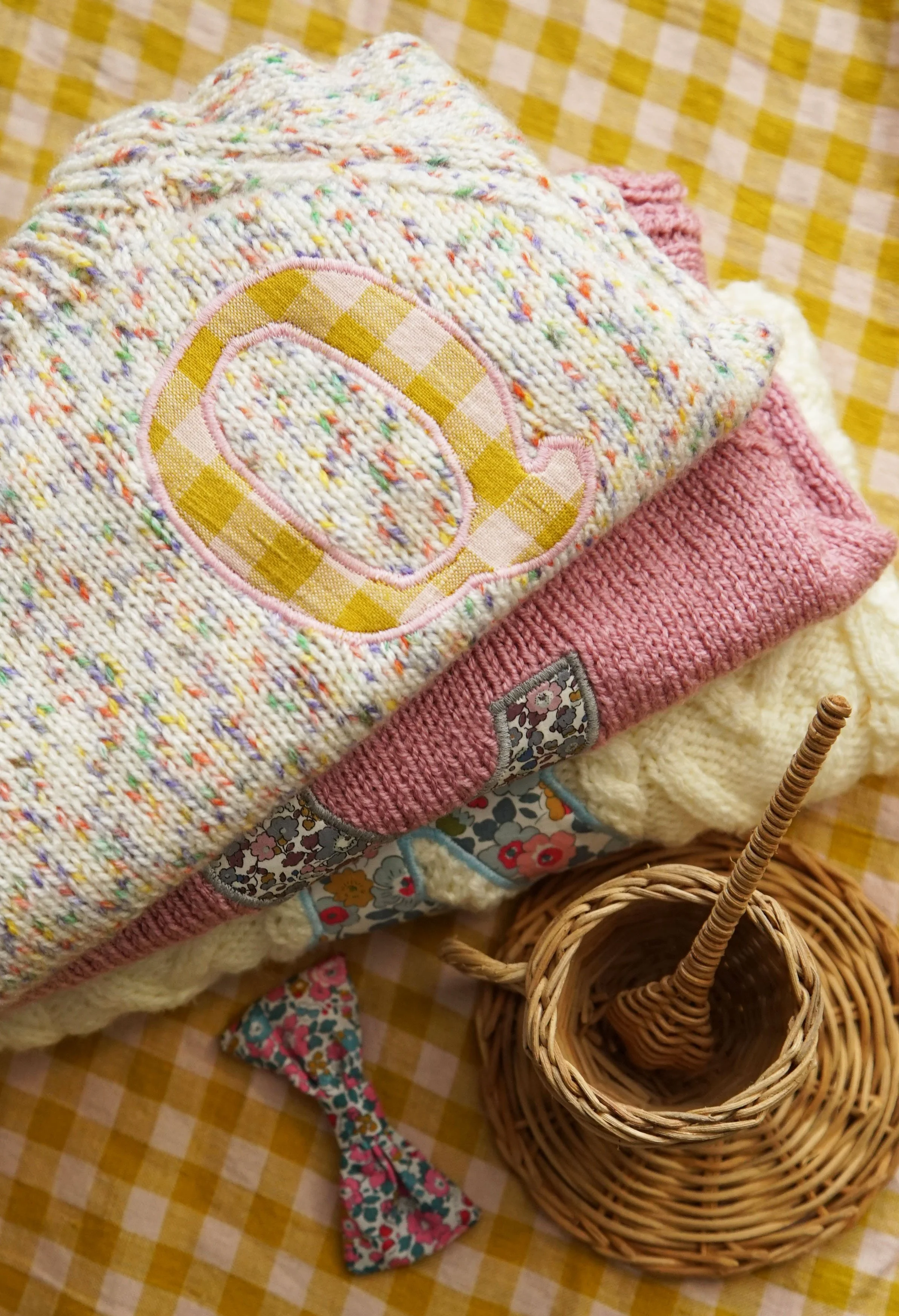 Stack of knitted baby clothes and a basket on a yellow gingham background.