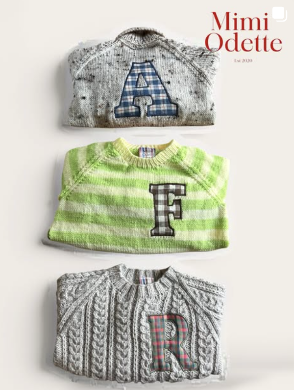 Three knitted baby sweaters featuring large letters A, B, and C. The left sweater is cream with an A, the middle is pink with a B, and the right is white with a C.