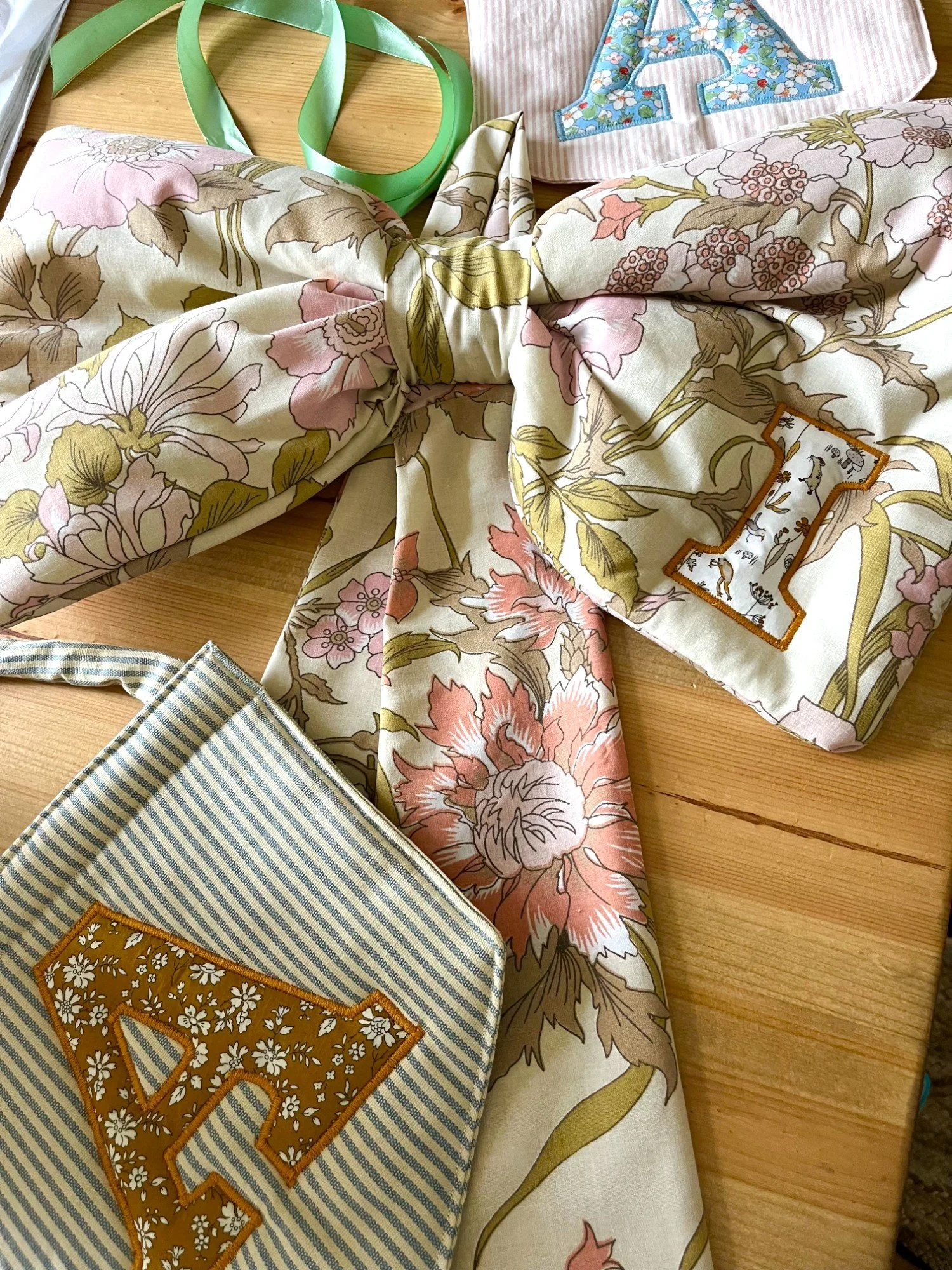 A floral patterned fabric tied into a bow, surrounded by decorative fabric patches with the letter 'A' on each, set on a wooden surface.