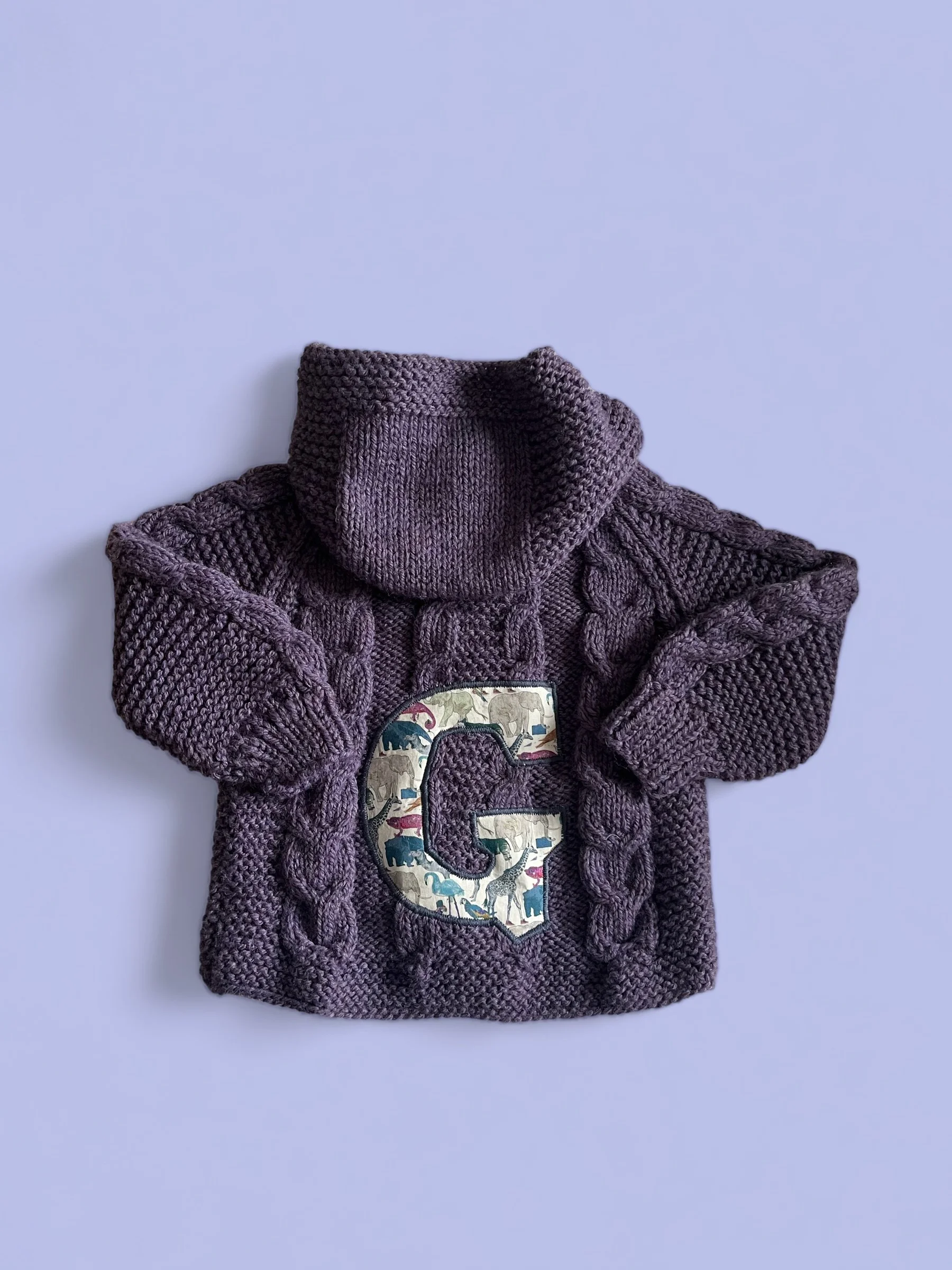 Purple knitted sweater with cable knit pattern and hood, featuring a large letter 'C' with a colorful zoo animal print in the center.