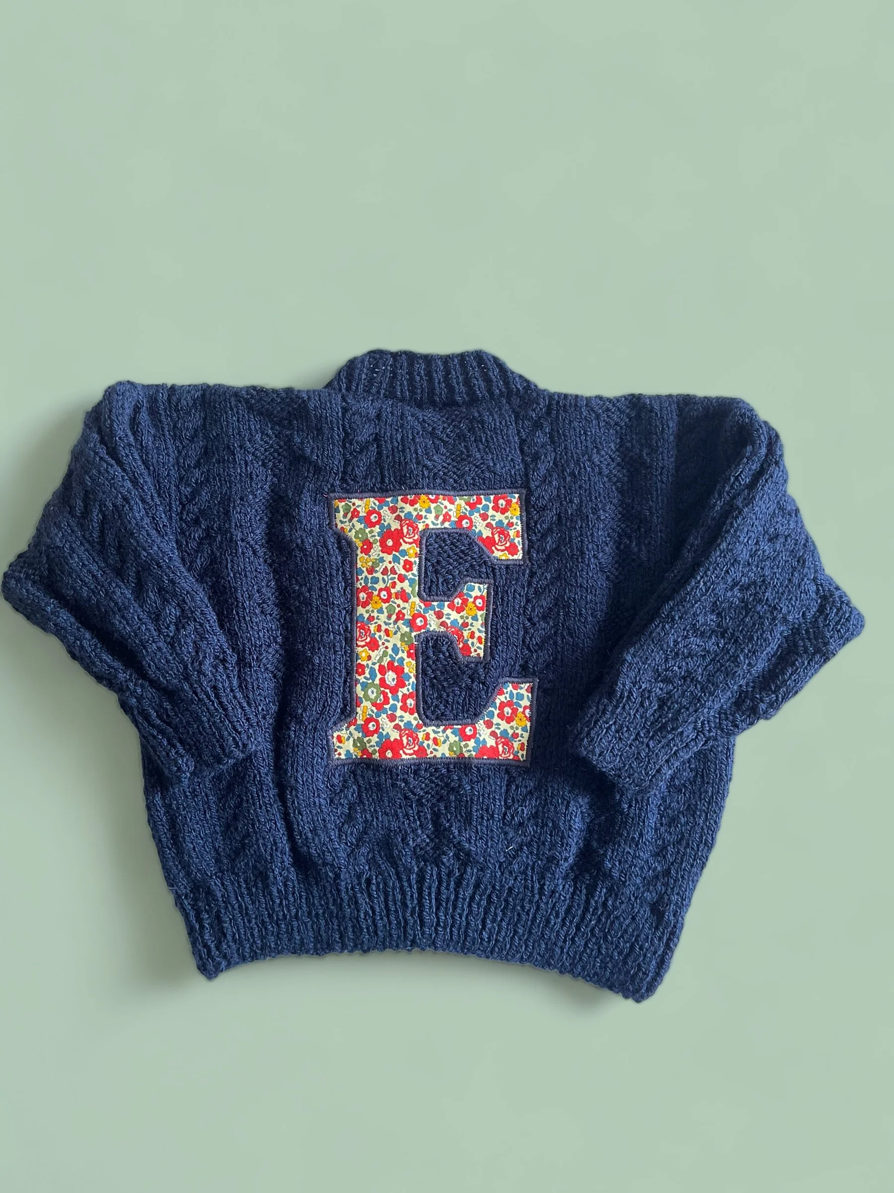 Blue knitted sweater with an embroidered letter 'E' in a floral pattern on the front.