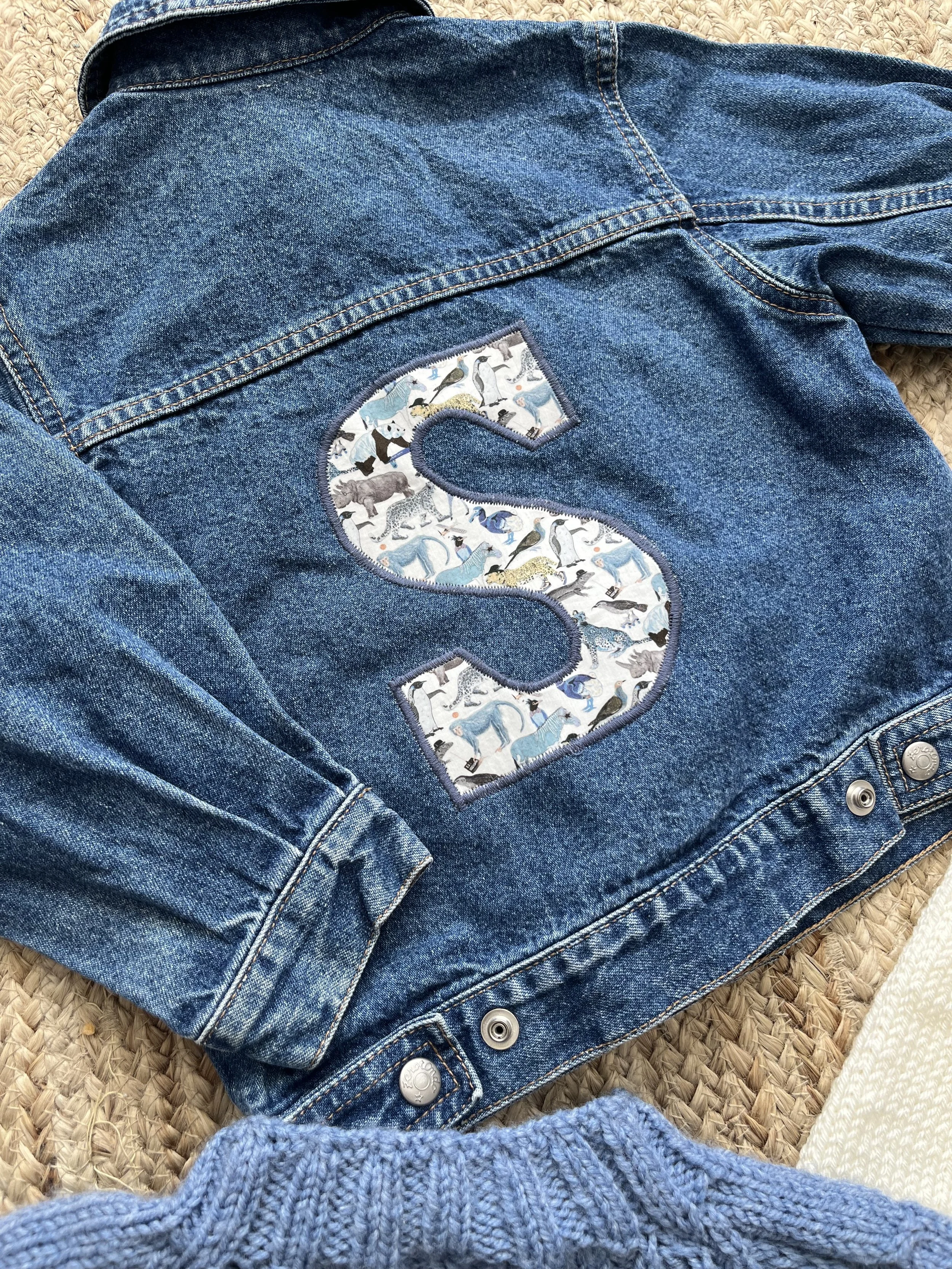 Denim jacket with large letter S patch on the back