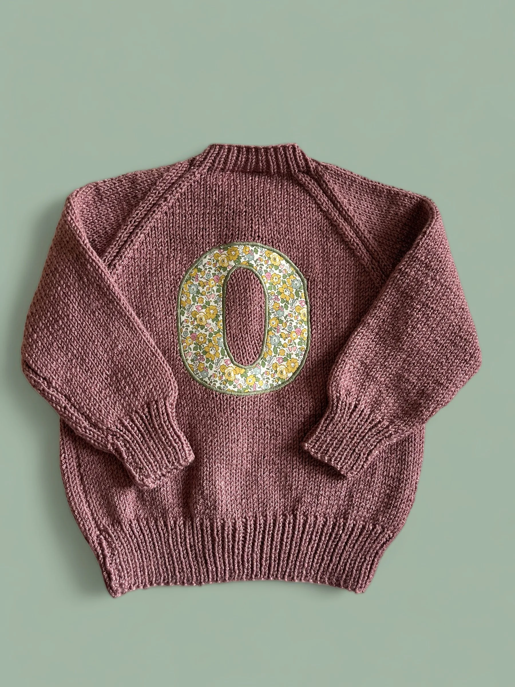 Pink knitted sweater with the number zero decorated with yellow flowers on the back