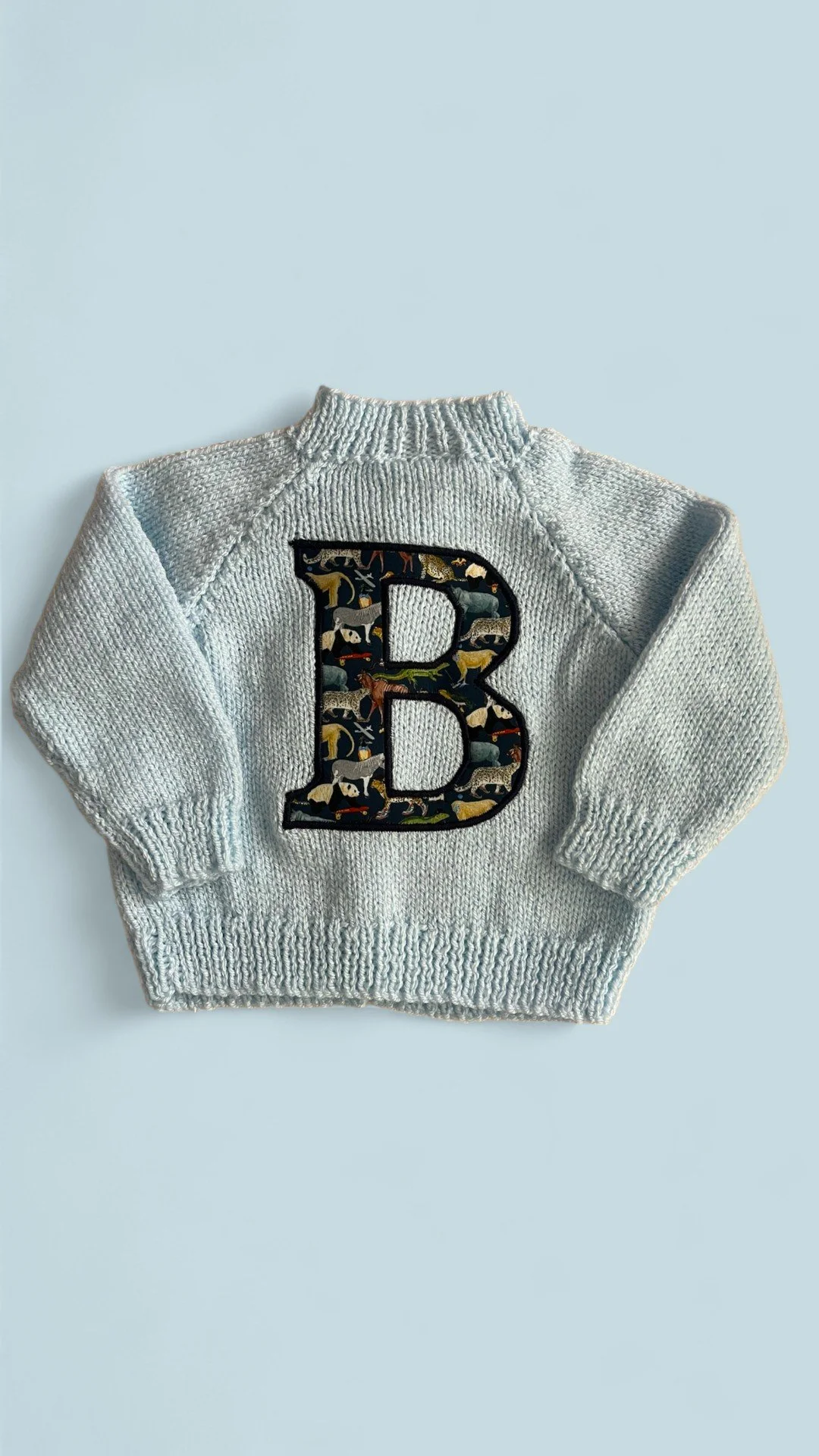 Light blue knitted sweater with a large letter "B" featuring animal patterns on the front.