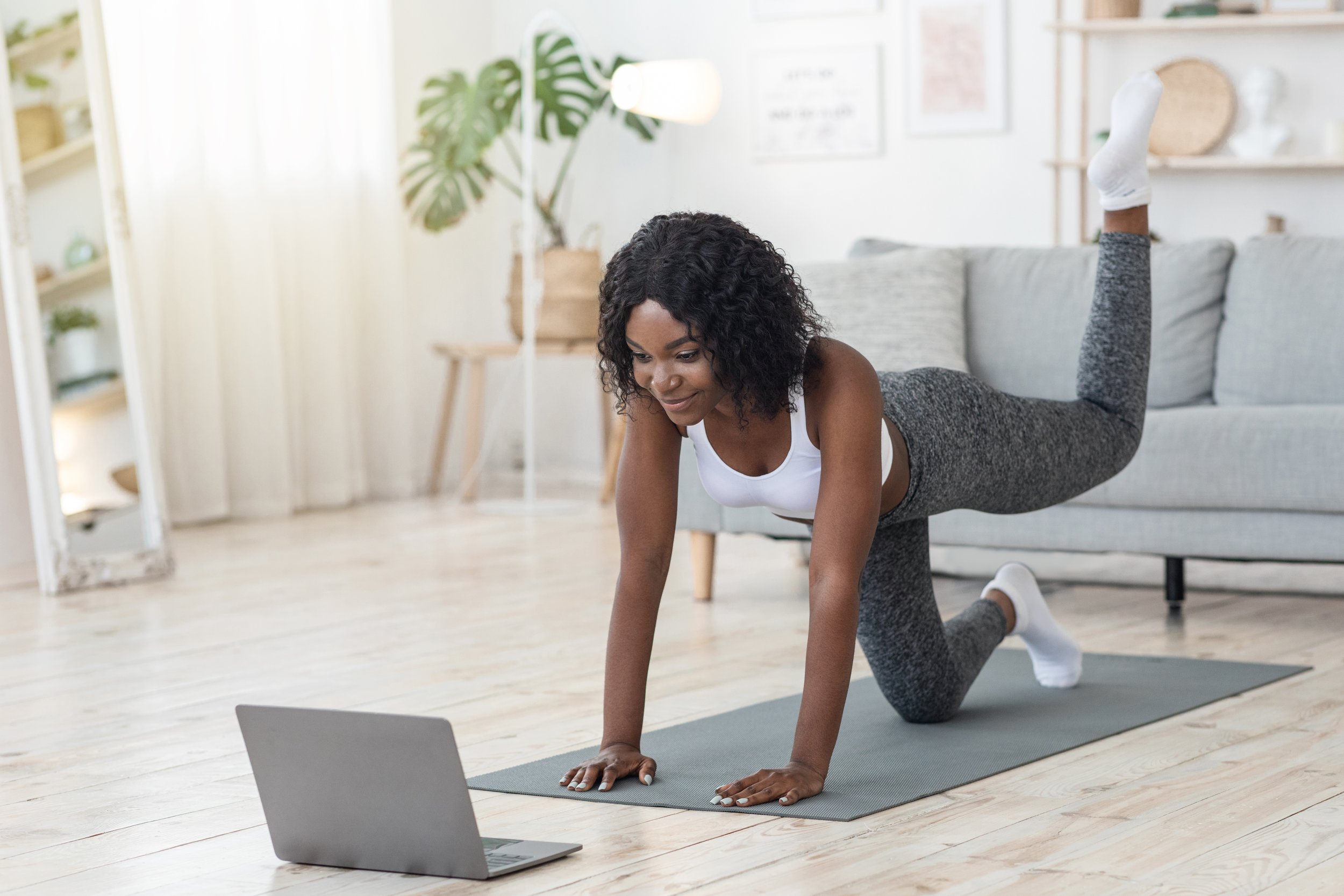Black woman exercising on floor with yoga mat and looking at a computer screen