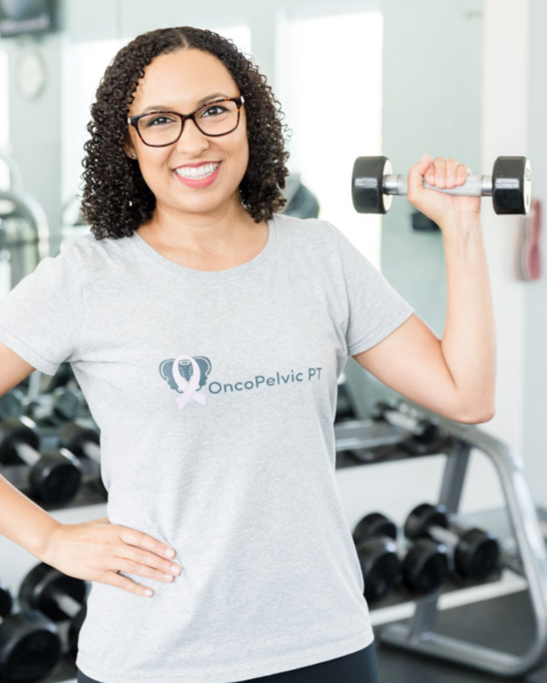 Dr Alex Hill smiling and wearing a gray  OncoPelvic PT t shirt, holding a weight